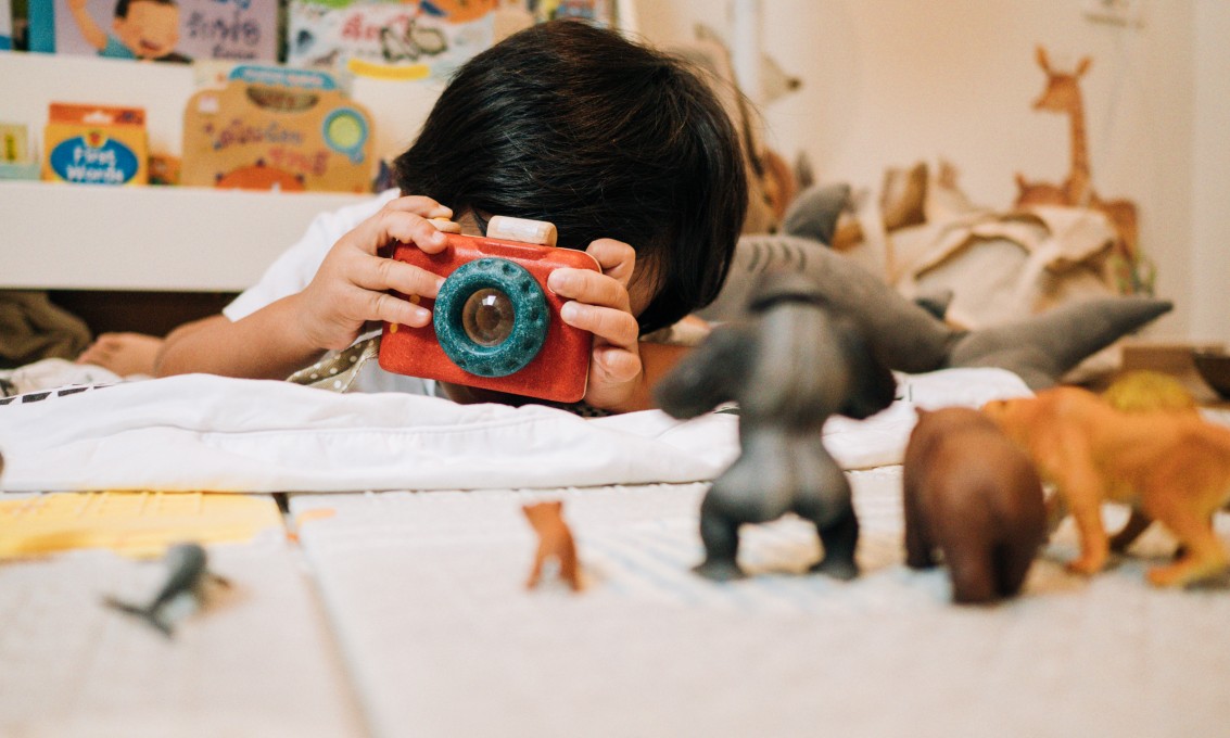 gutt holder et lekekamera opp til øynene og tar bilder av lekedyr