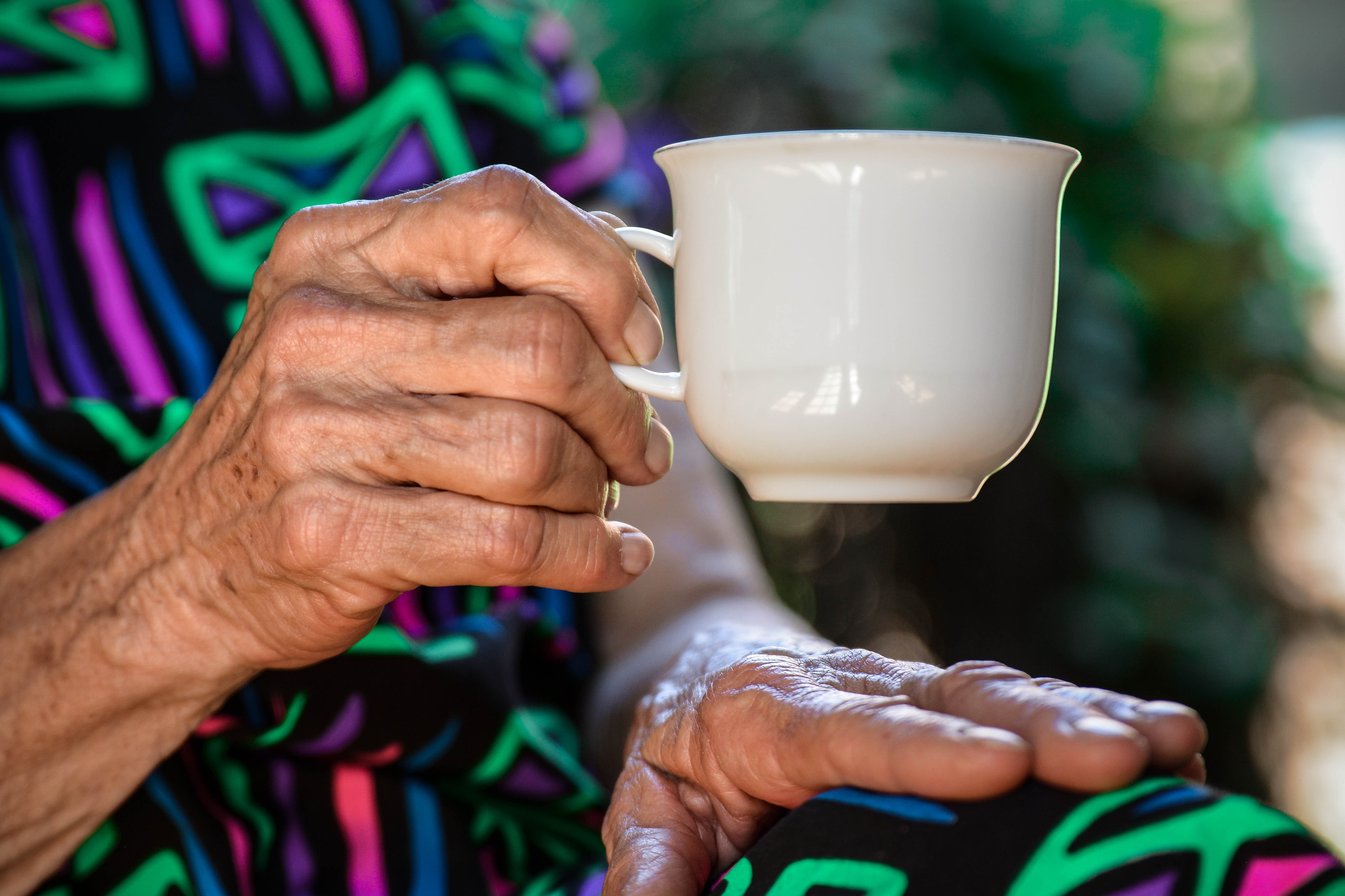 En eldre kvinne sitter og holder en kaffekopp.