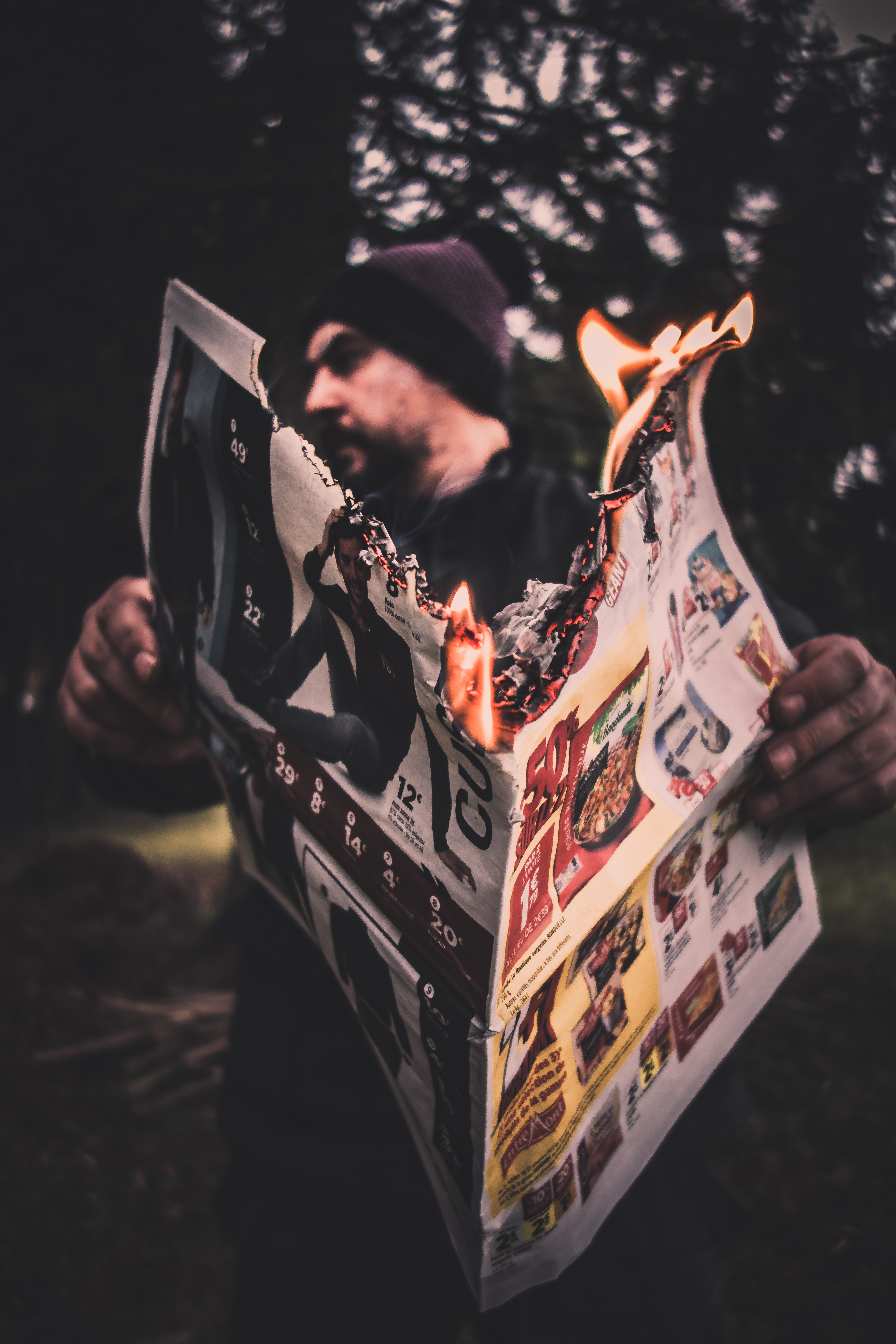 En mann med lue holder en åpen, brennende avis.