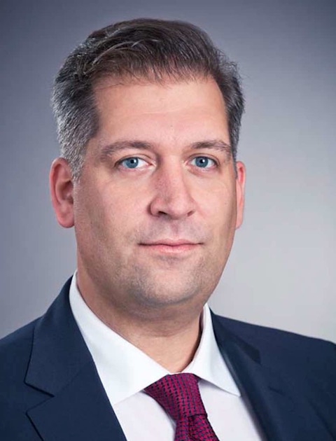Associated professor at the University of Stavanger, and project leader Thomas Michael Sattich. A middle-aged man with dark hair with hints of grey, eye contact, blue eyes and suit. White shirt with a pink-burgundy colored tie with blue crosses. 