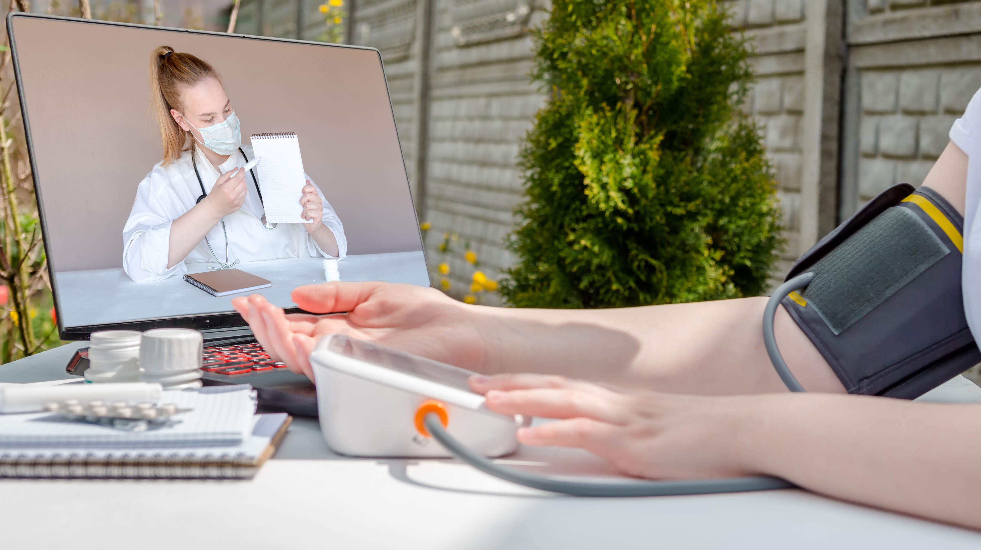Person måler eget blodtrykk med oppfølging av helsepersonell digitalt på en skjerm.