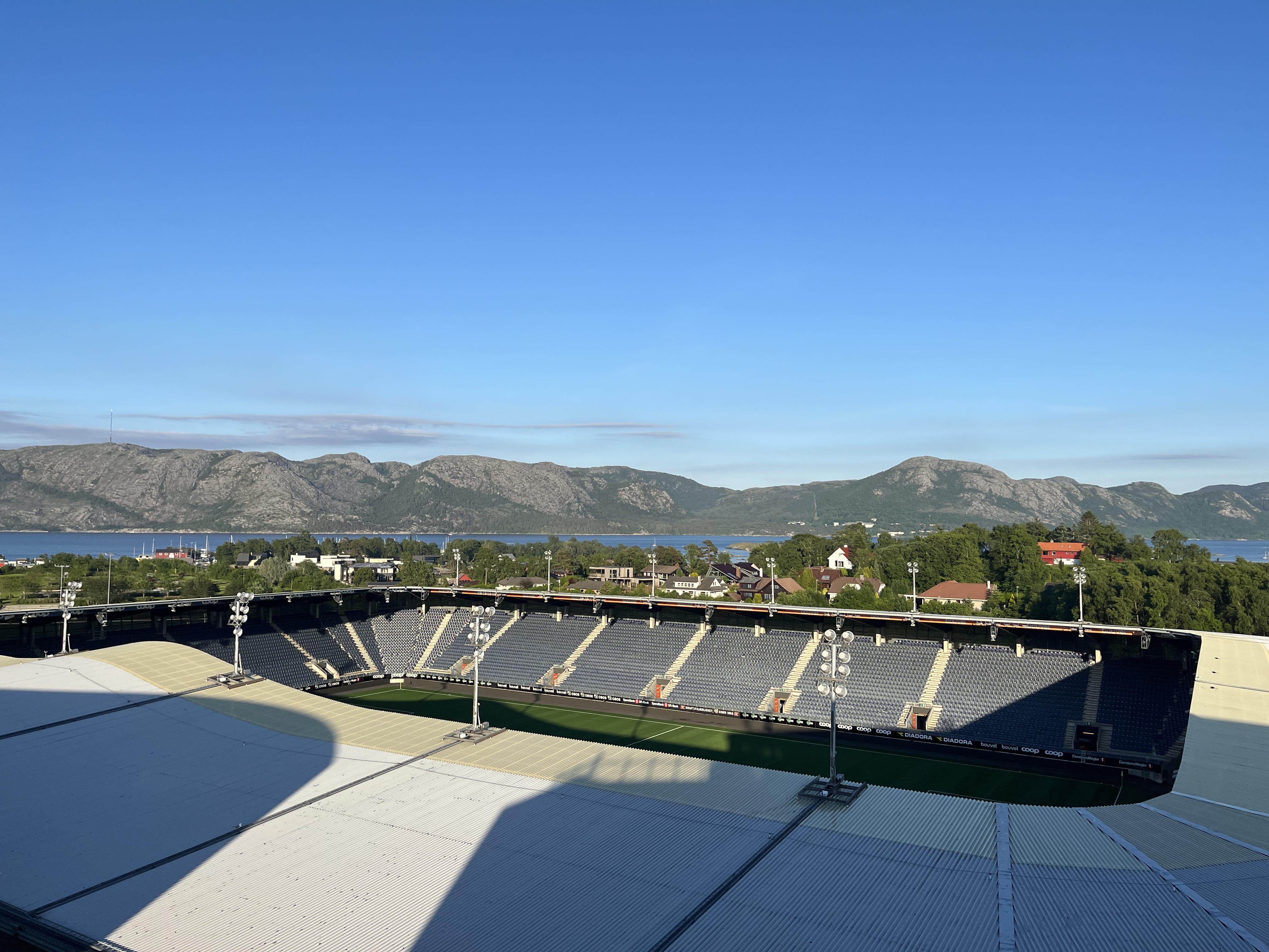 Fotballbane sett ovenfra med fjord og fjell i bakgrunnen. Foto