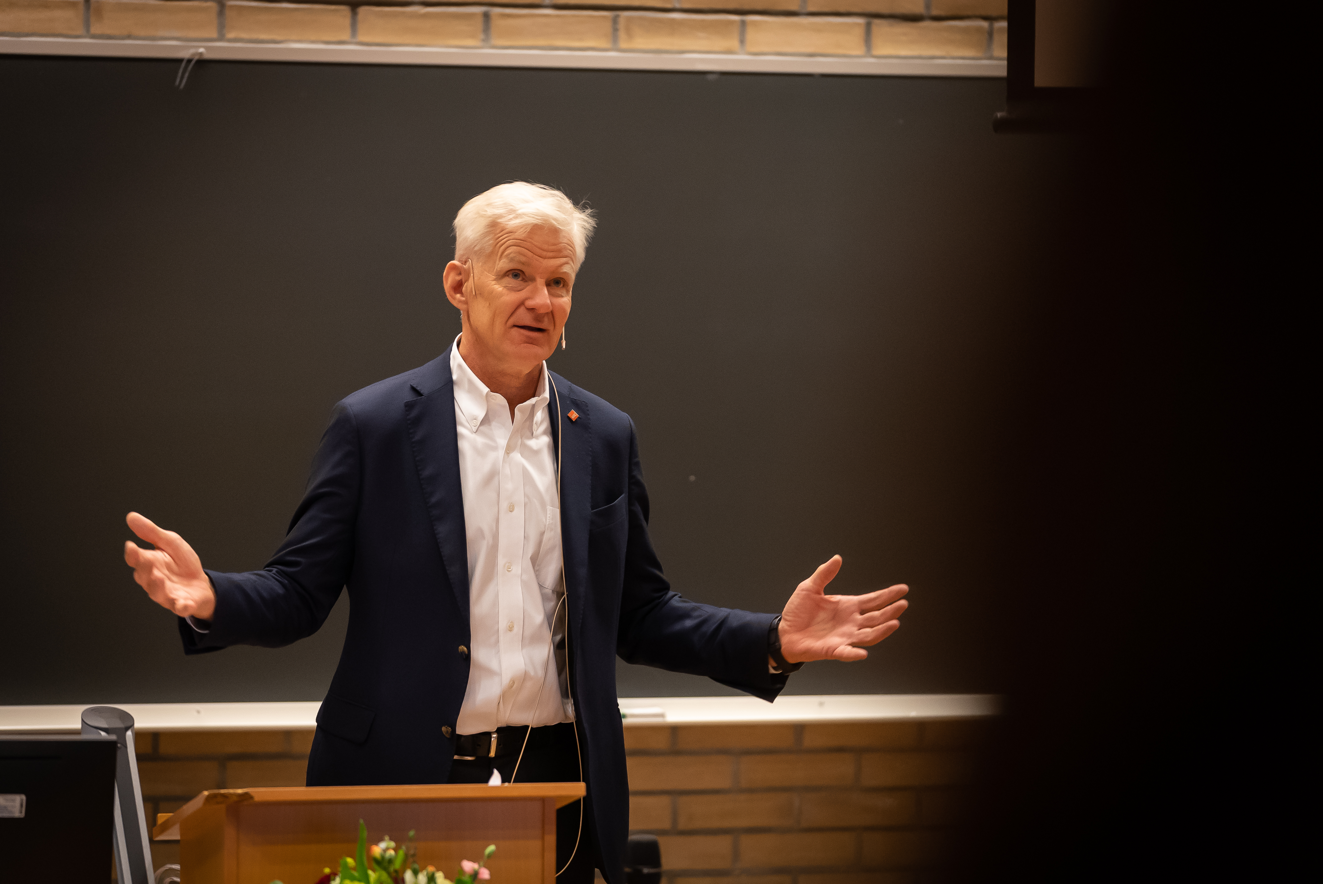 Mann som gestikulerer under et foredrag foran en talerstol