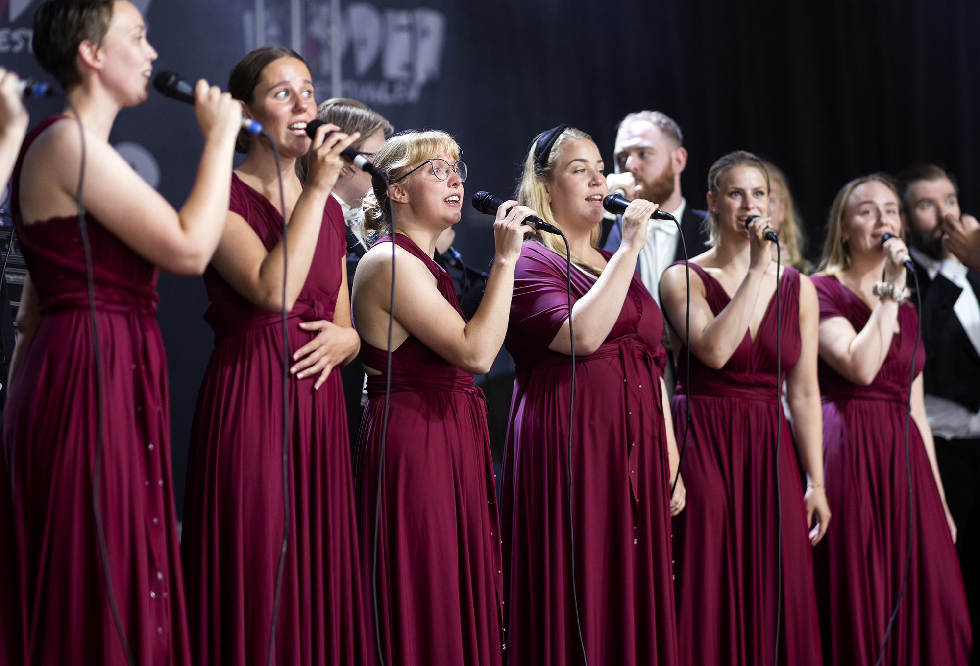Kvinnelige sangere i mørkerøde kjoler står på rekke og synger