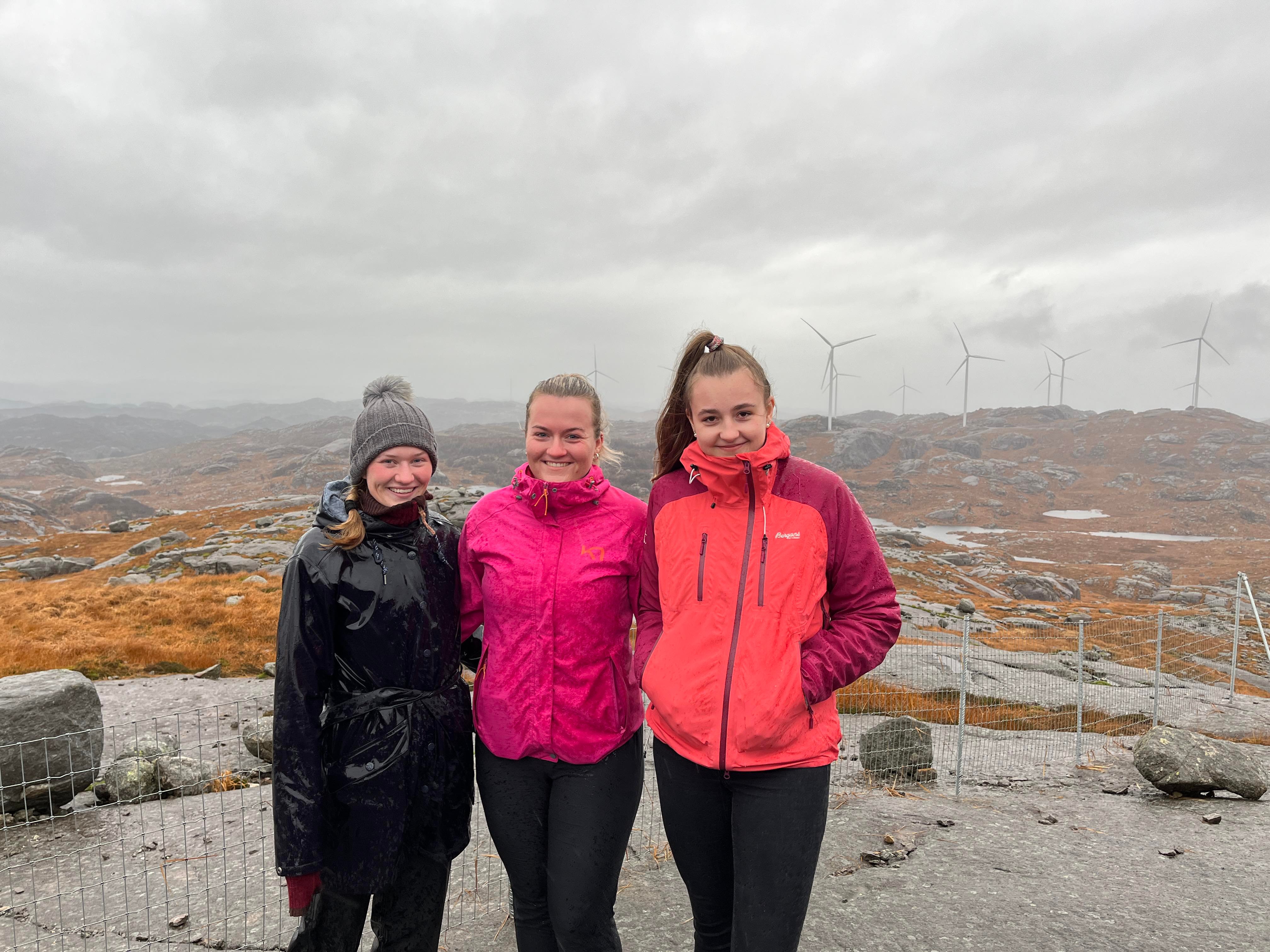 Studentane Ingrid Flood, Ragnhild Leidland og Maren Lovise Jåsund foran vindparken i Bjerkreim i grått vær