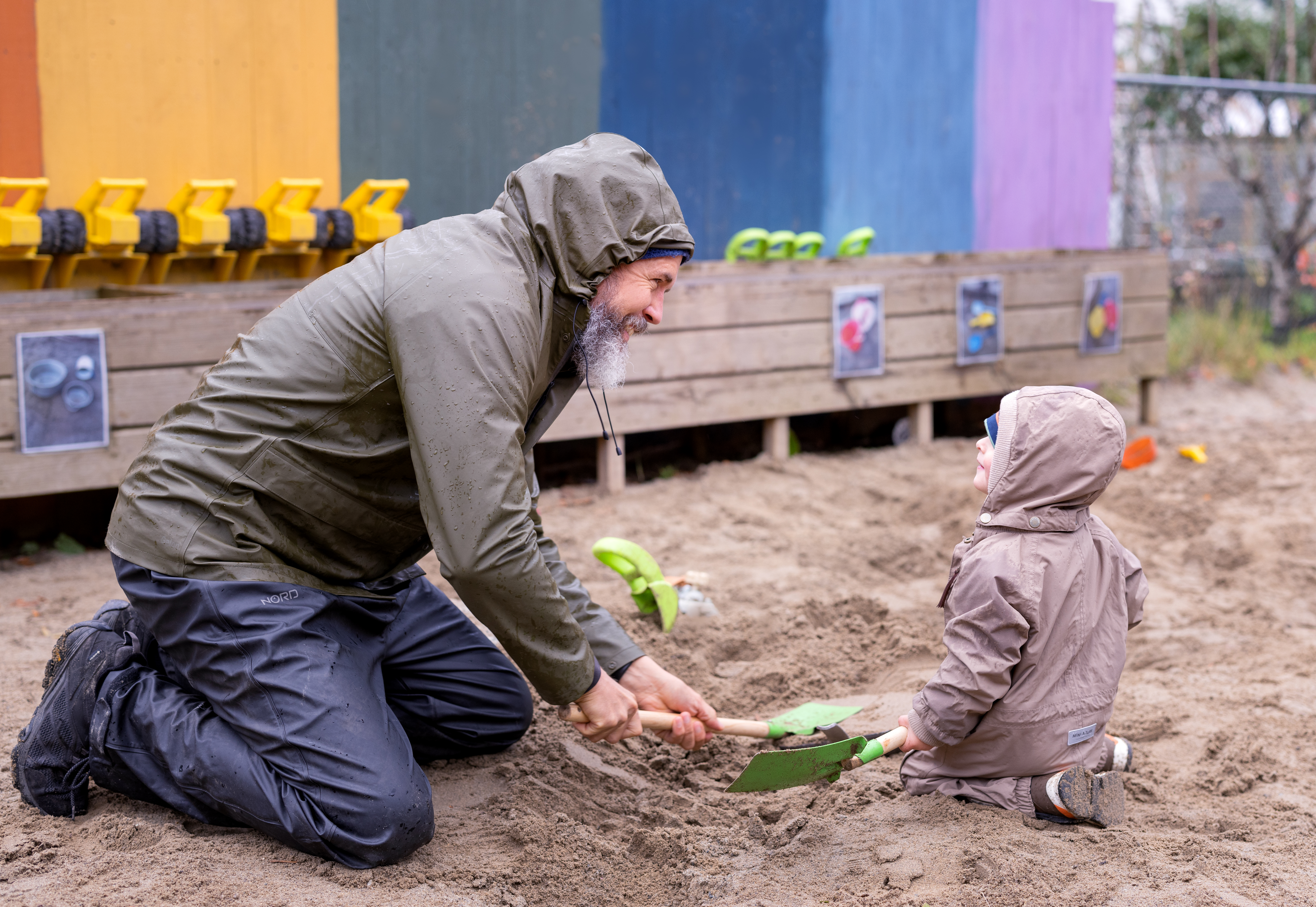 En voksen og et barn leker i sandkassen på en regnfull dag. Foto: Elisabeth Tønnessen/Læringsmiljøsenteret, UiS