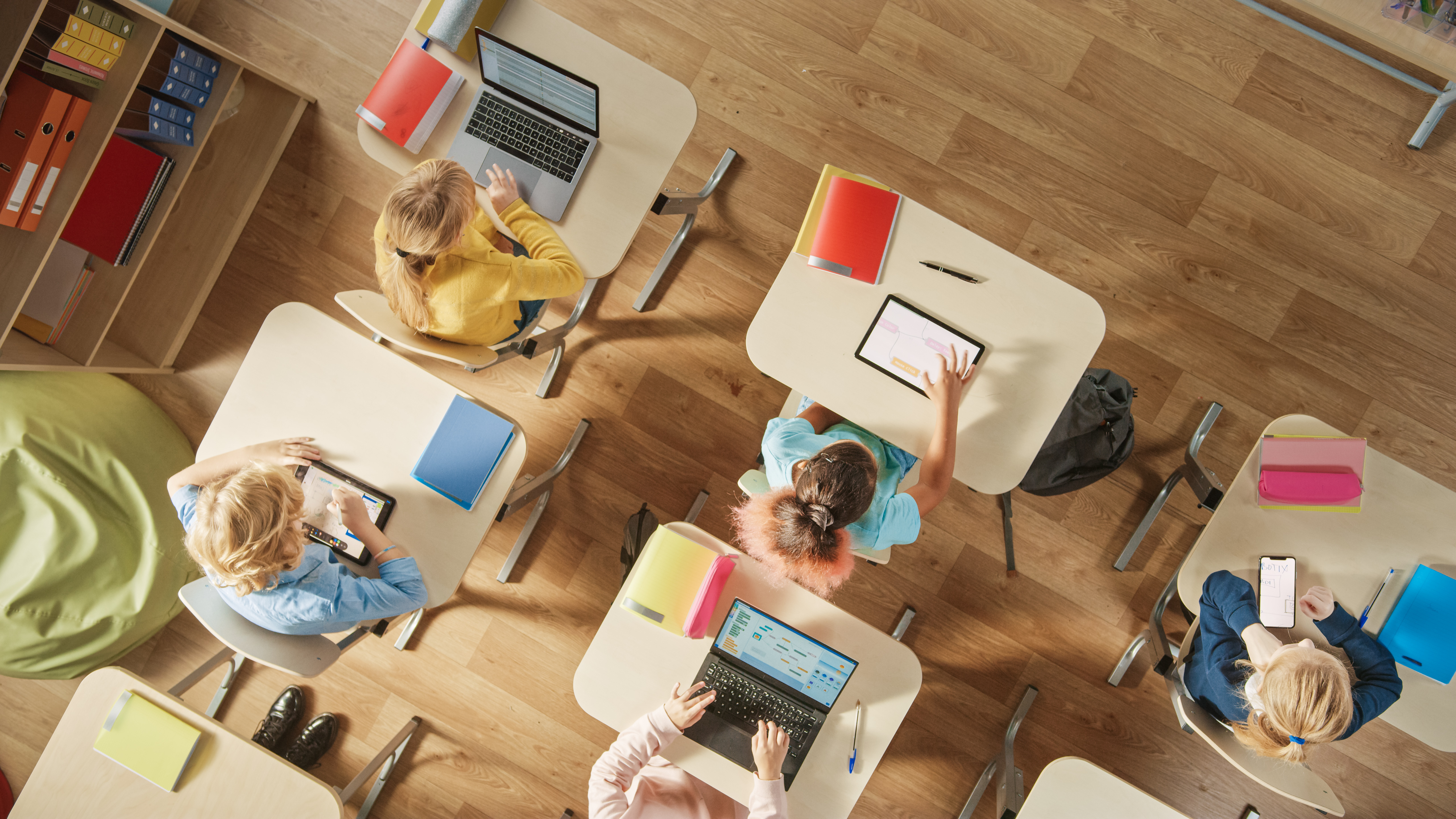 Toppvisningsbilde i klasserommet på barneskolen: Barn som sitter ved skolepulten ved hjelp av personlige datamaskiner og digitale nettbrett til oppgaver.