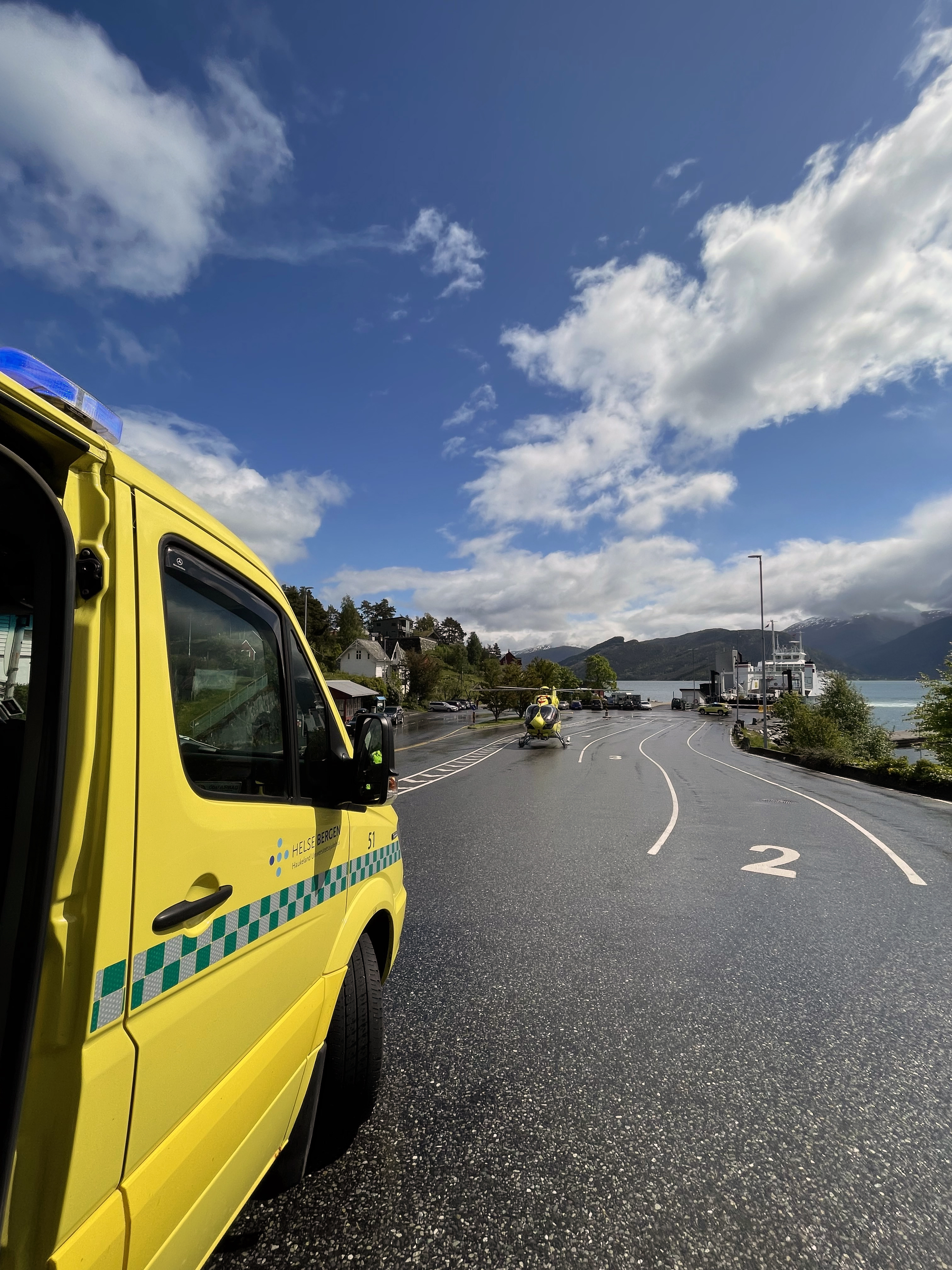 Ambulansebil i naturlige omgivelser med et helikopter i bakgrunnen