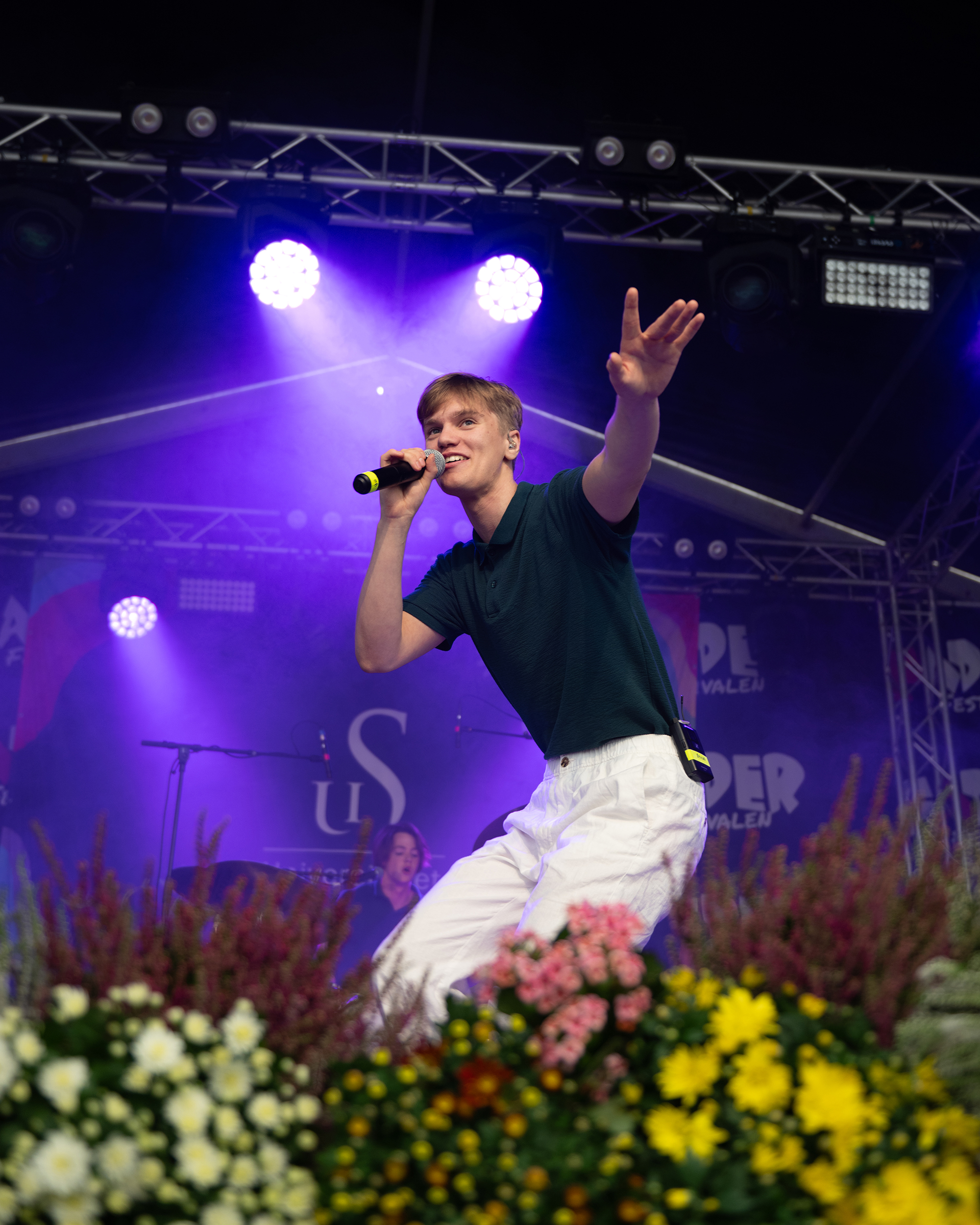 Ung sanger med mikrofon på scene med blomster i forgrunnen