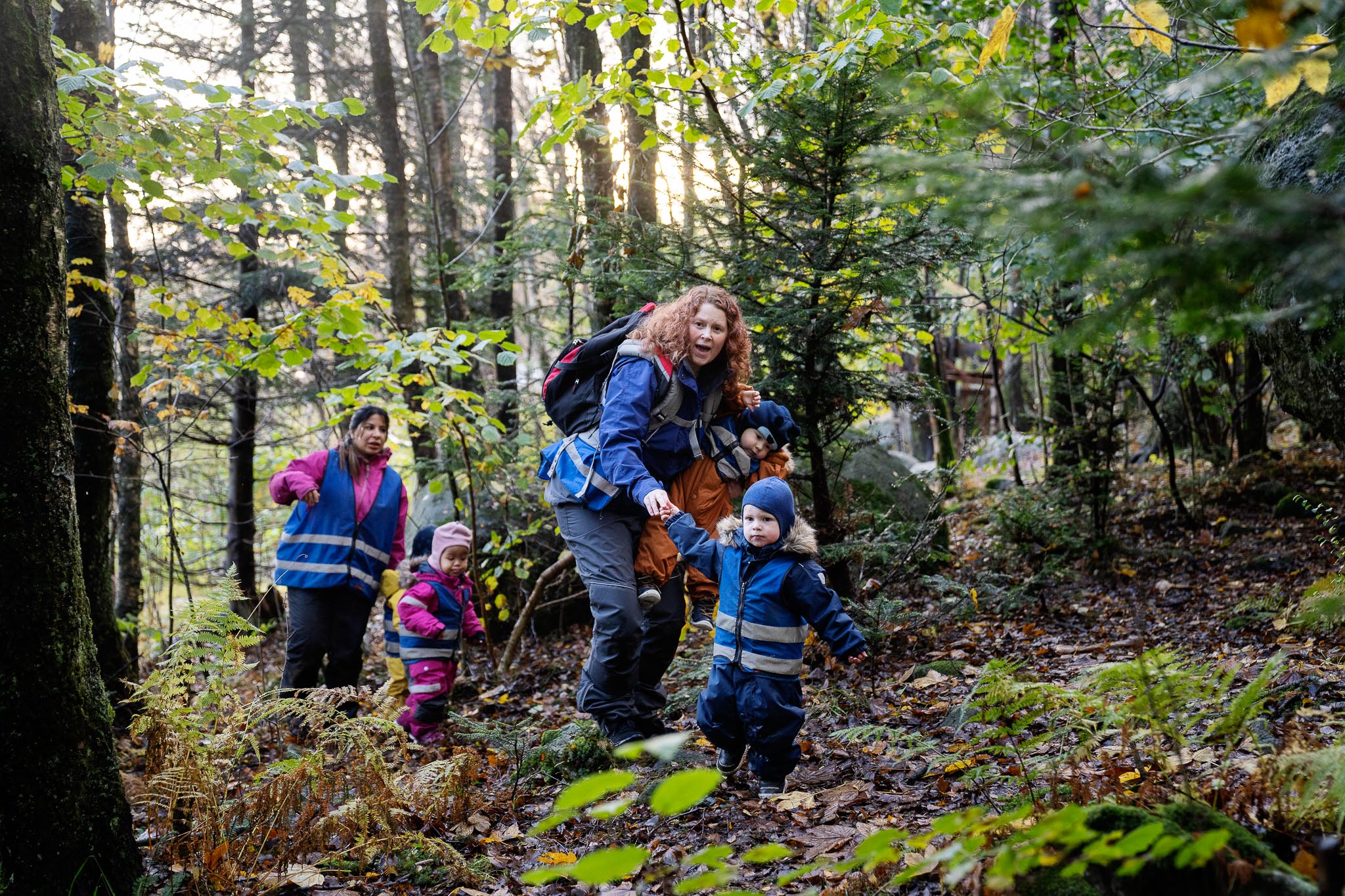 To barnehagelærerer og tre barn med refleksvest på oppdagelsestur i naturen.