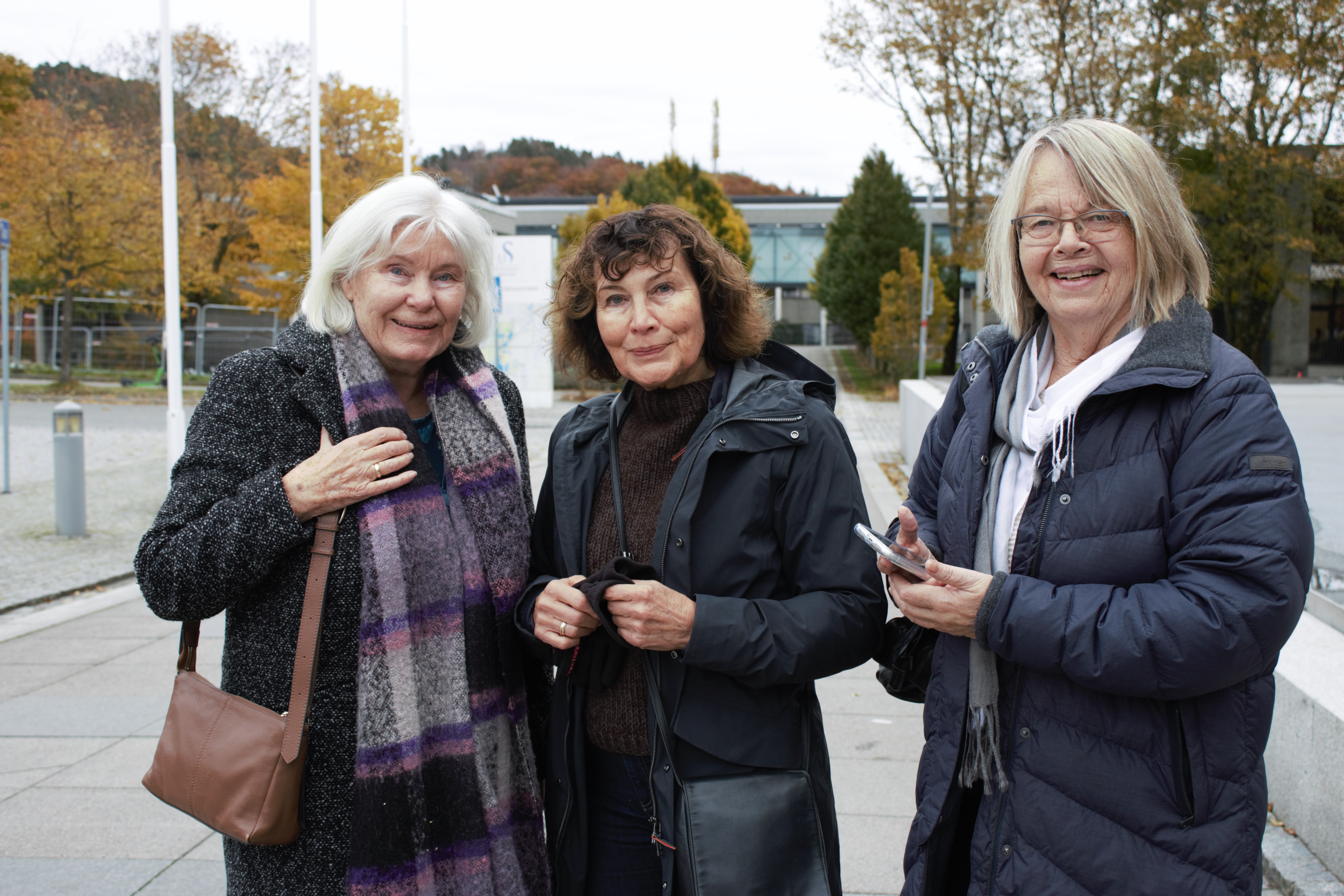 tre kvinner ute på en åpen plass smiler til kamera