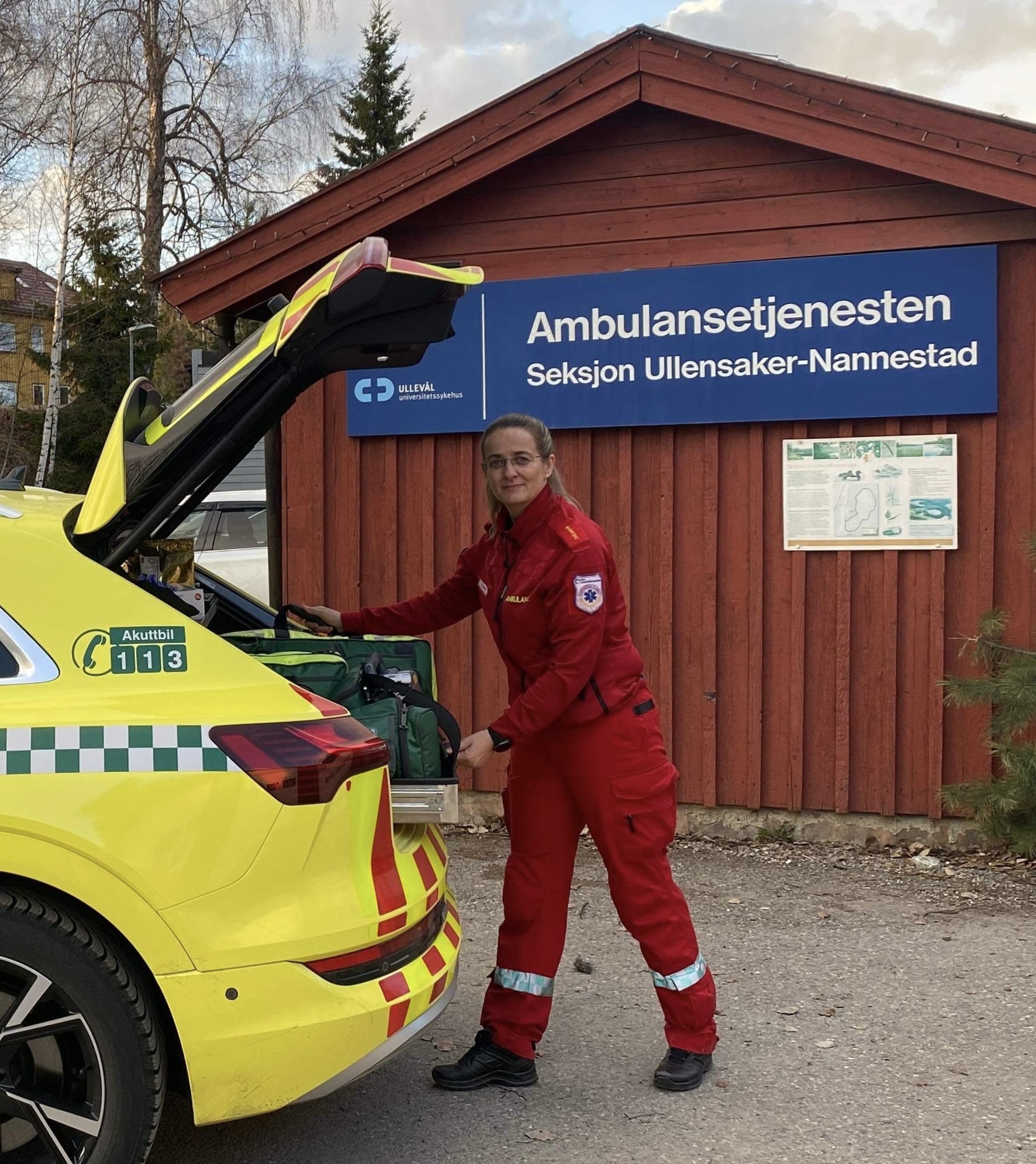 Kvinne i ambulanseuniform legger utstyr i bagasjerommet til en legebil