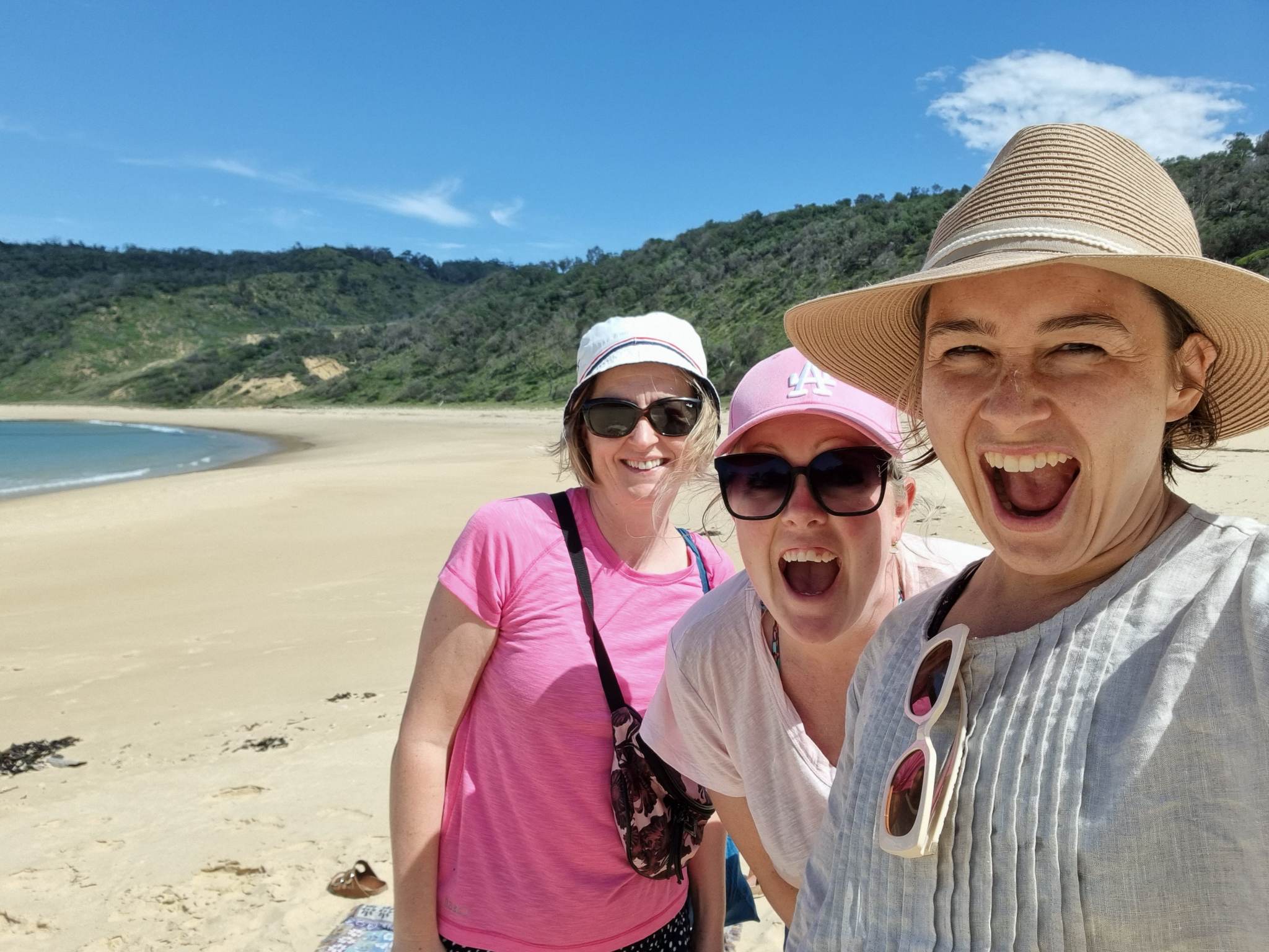 Tre kvinner på stranden smiler til kamera