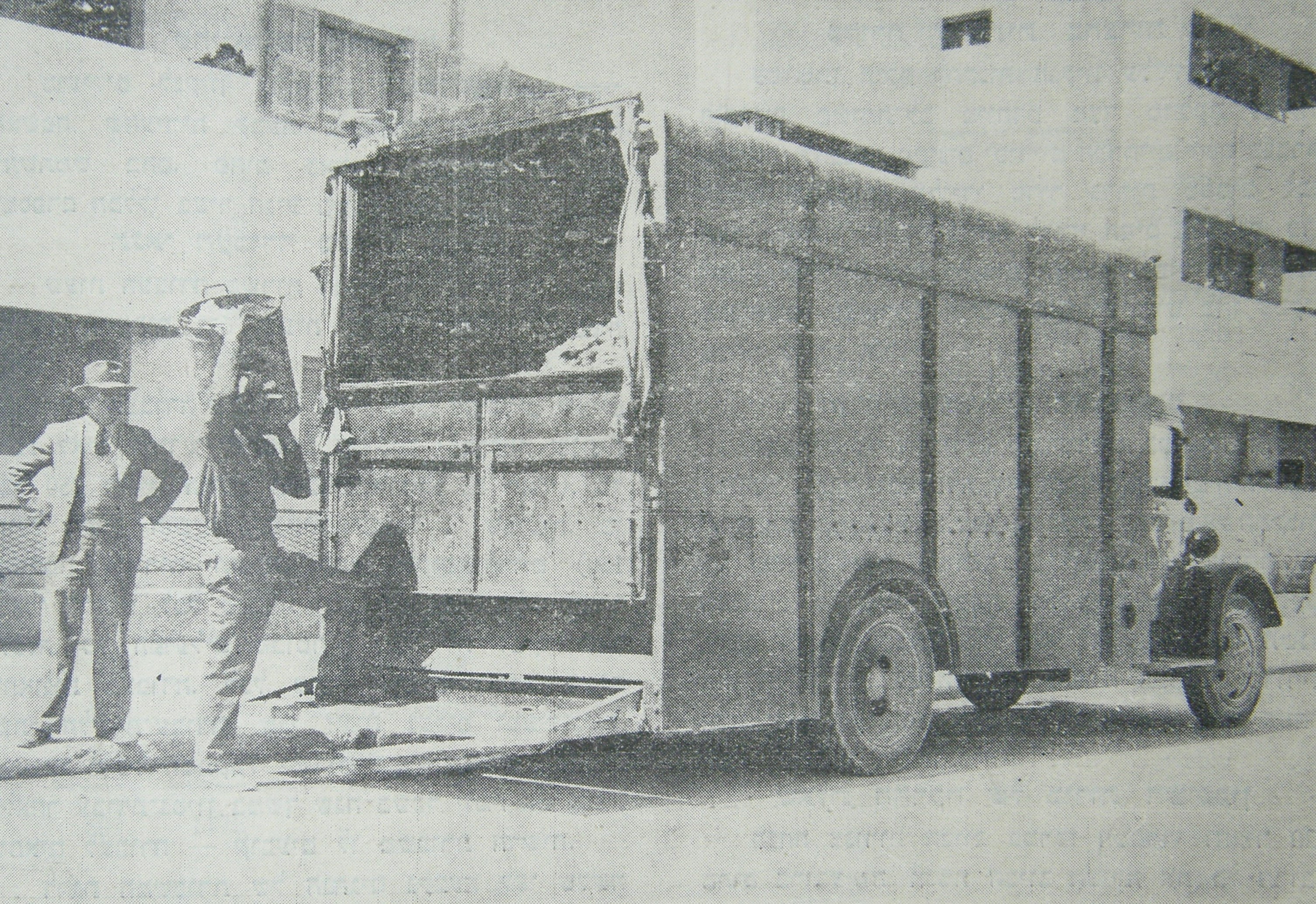 A garbage truck with one person loading rubbish into it and another watching