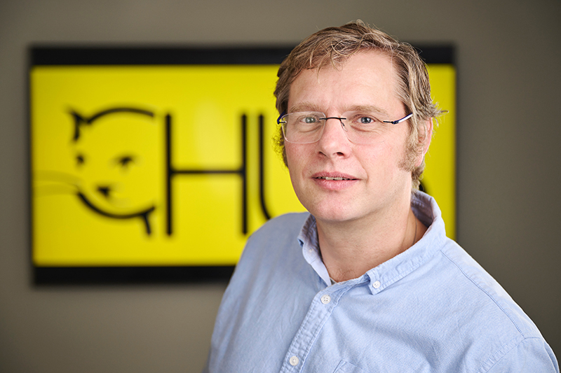 Mann med briller foran et gult og svart skilt.