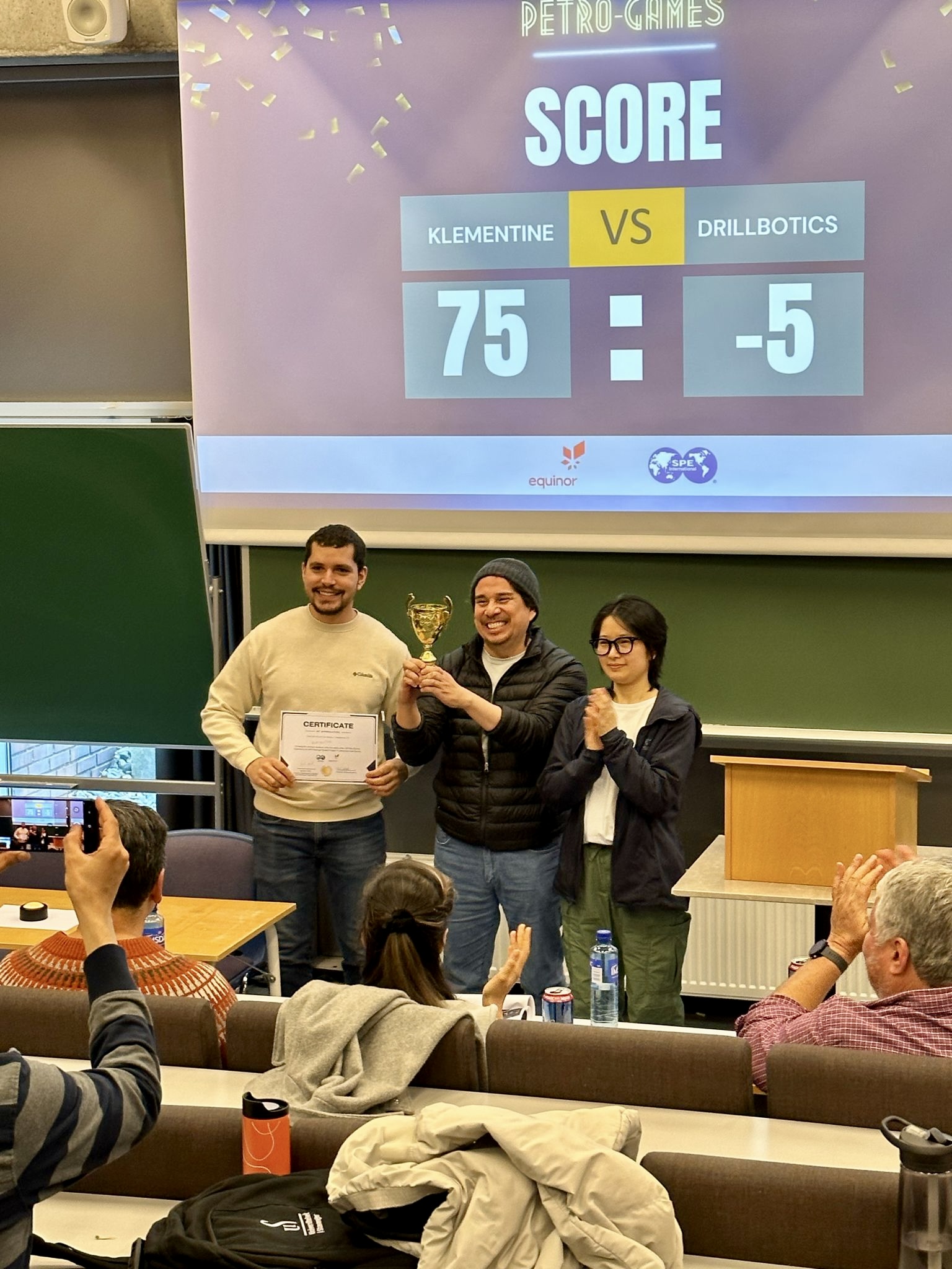 Tre studenter holder en pokal og jubler.