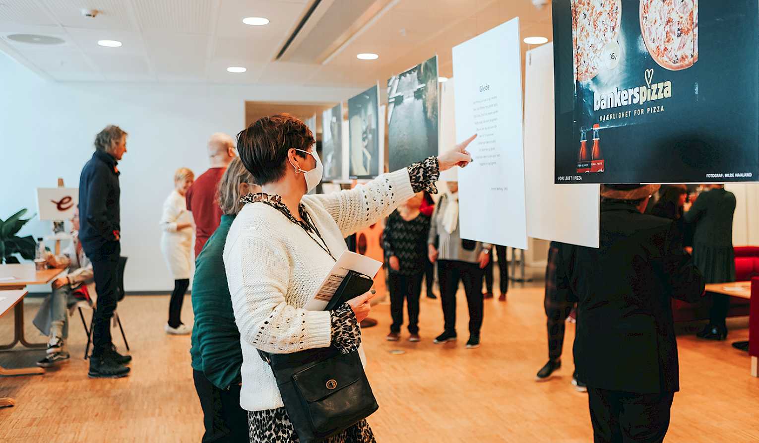 En gruppe mennesker studerer bilder i et utstillingslokale