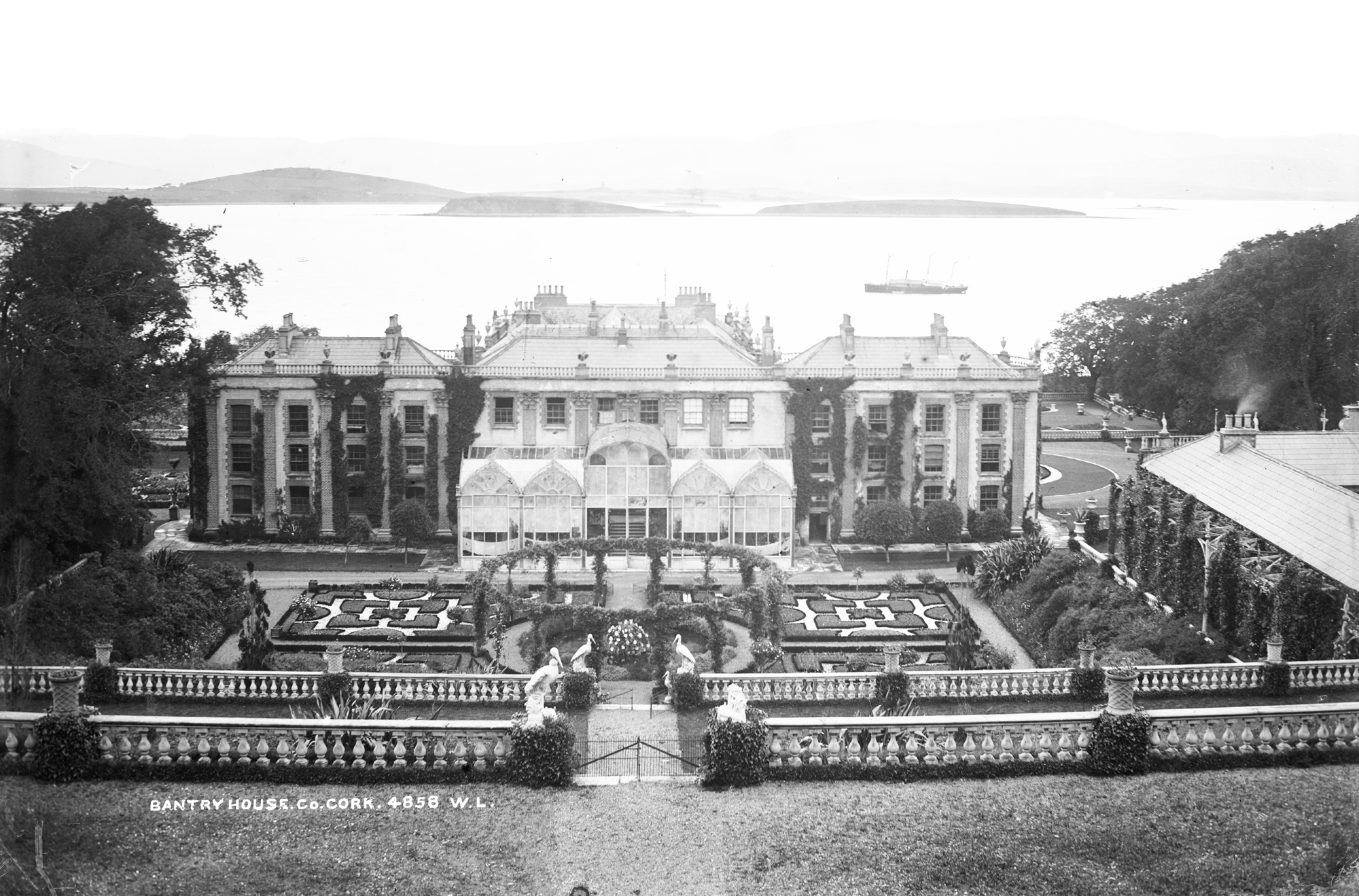 A black and white image of a coutnry house with formal gardens laid out in front of it