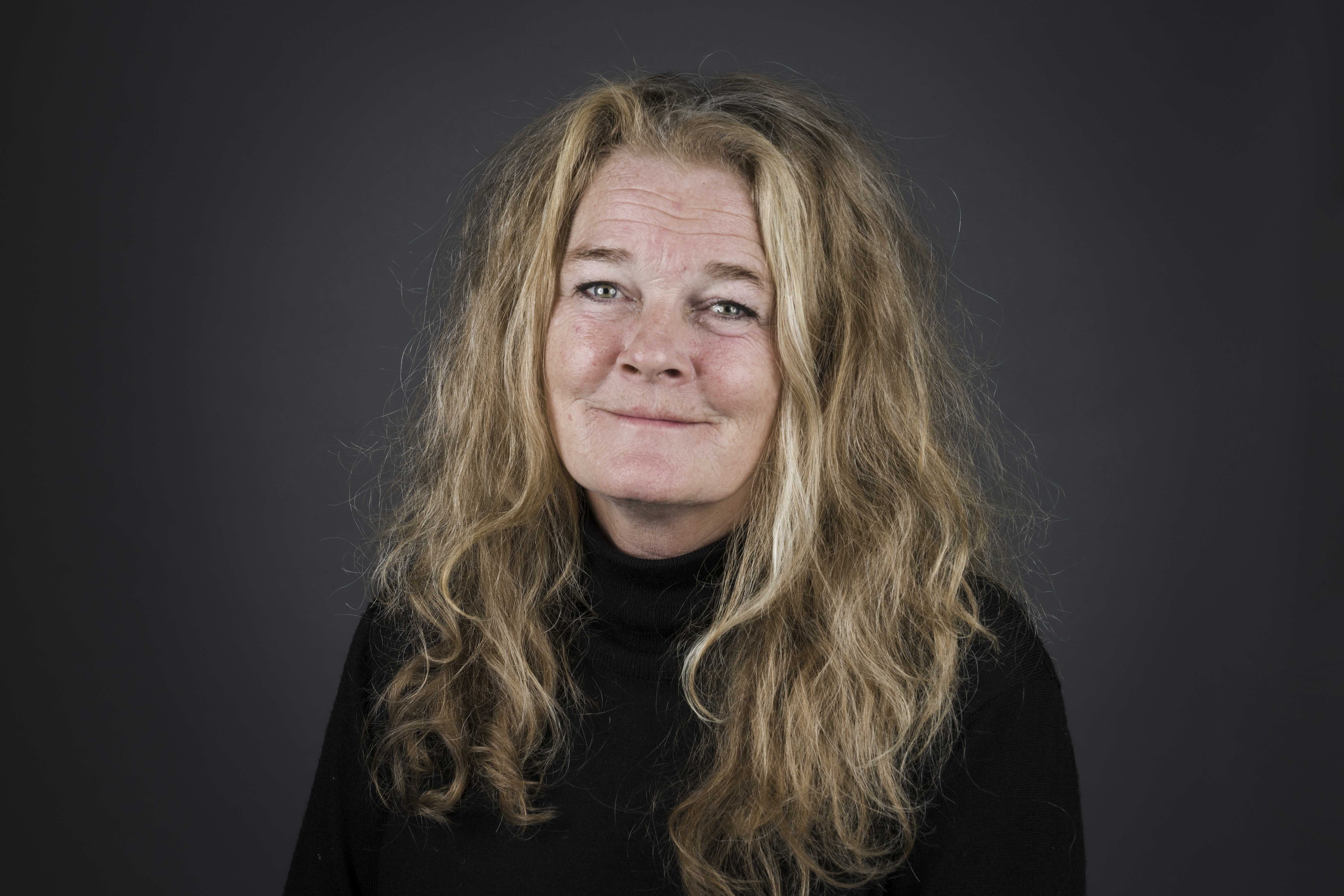 Kvinner smiler til kamera. Mørk bakgrunn.