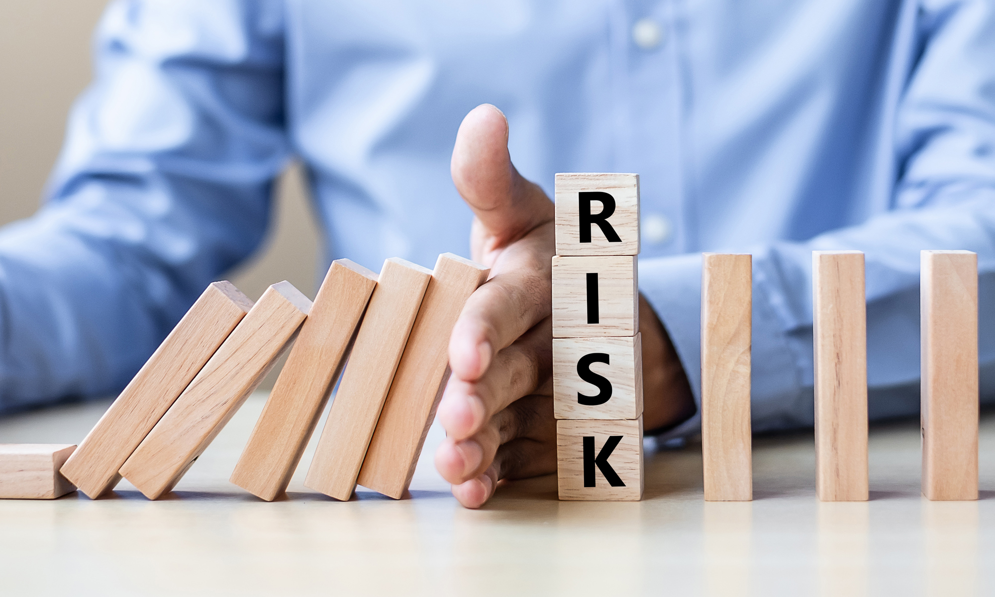 Mann som stopper domino fra å falle, med noen terning med bokstaver RISK der hånden er plassert. Bildet illustrere at man hindre mer ulykker der risiko inntreffer.