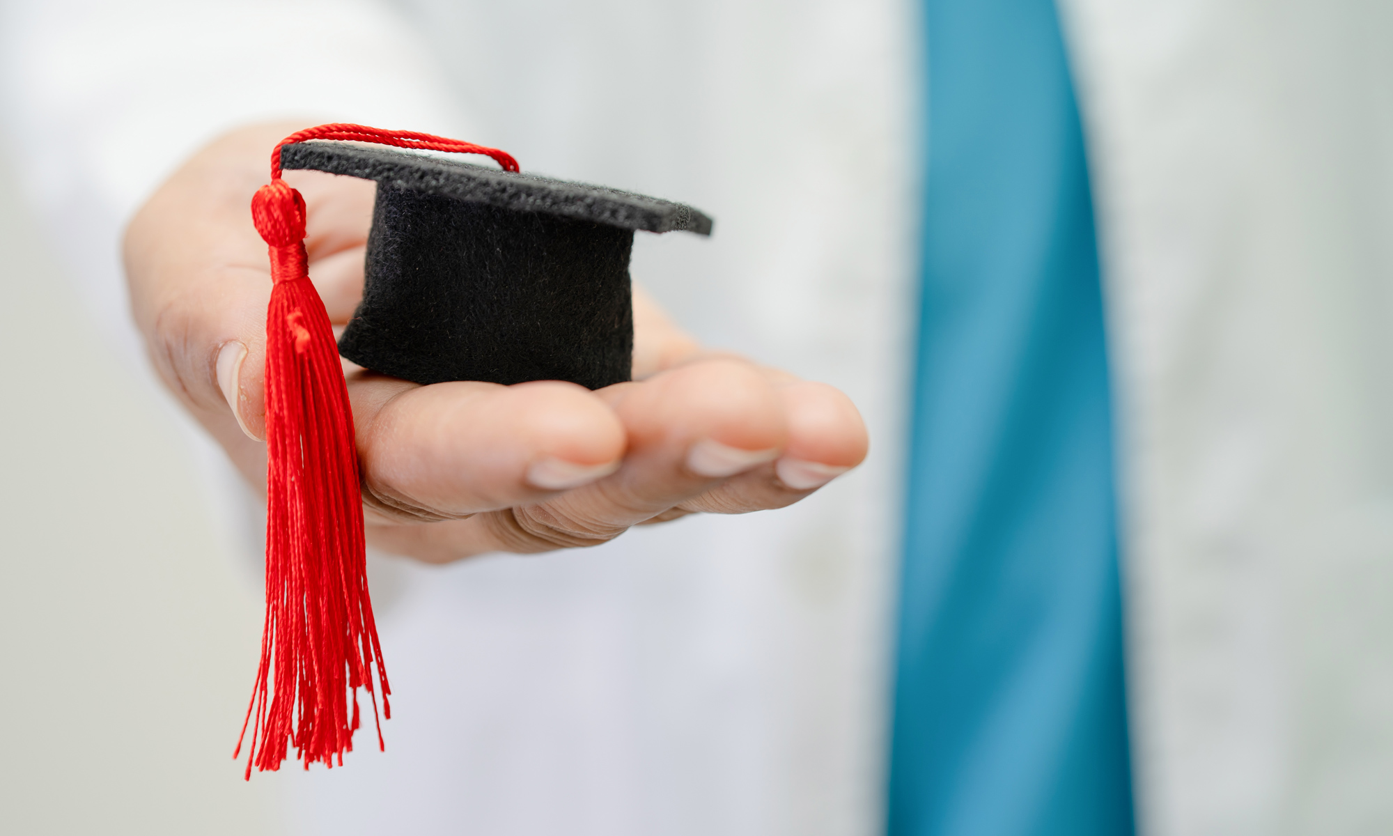 Graduation cap, held by a student in white shirt and tie.