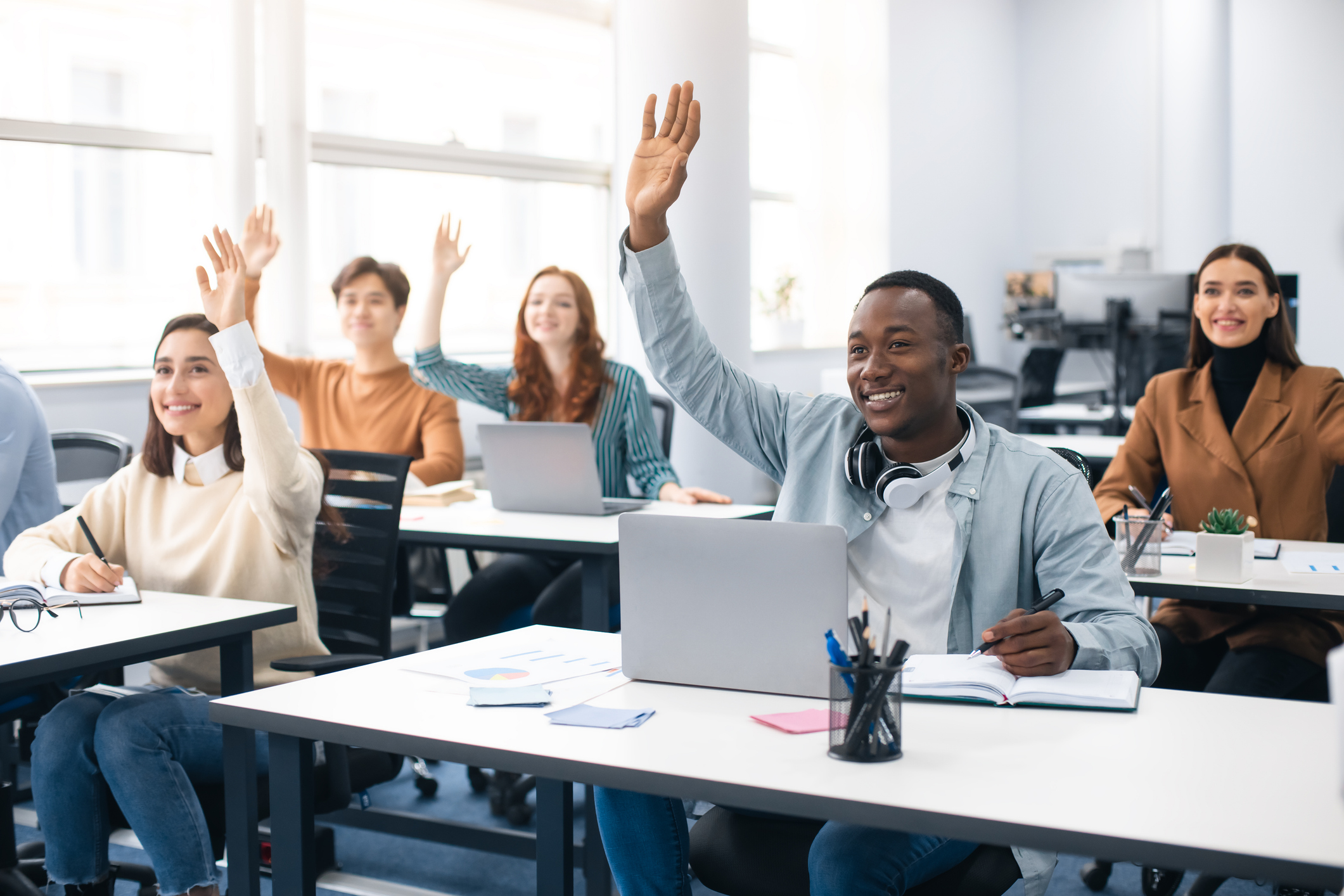 Voksne studenter i klasserom rekker opp hendene
