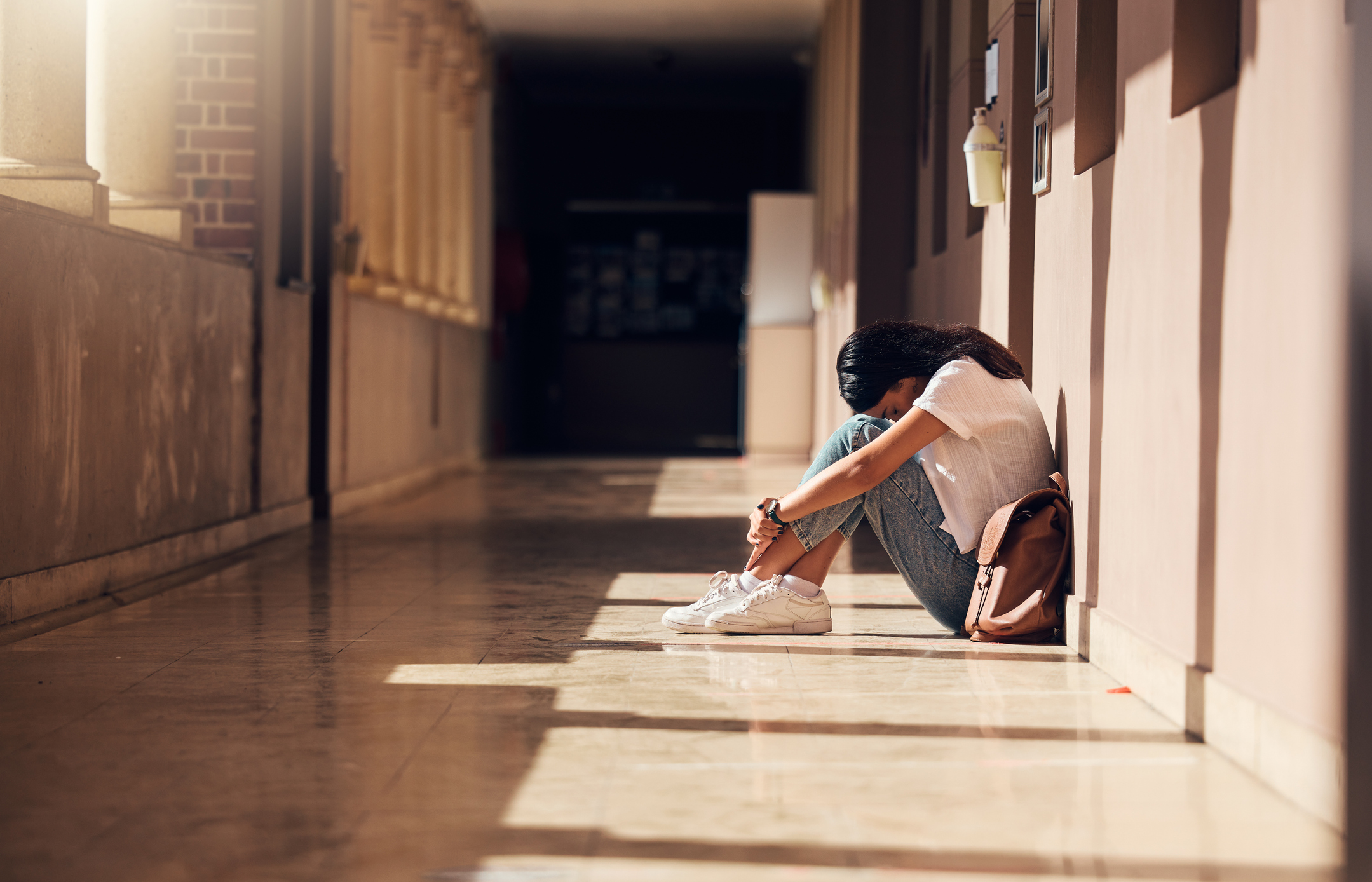Jente sitter  gangen med hode inntil knerene. Sekken er på siden av hene