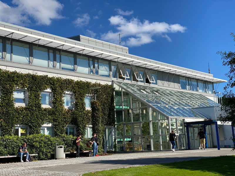 Bygningsfasade med eføy, med studenter på benker utenfor