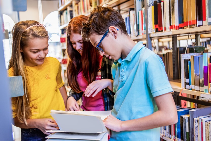 En gutt og to jenter leser i bok i et bibliotek
