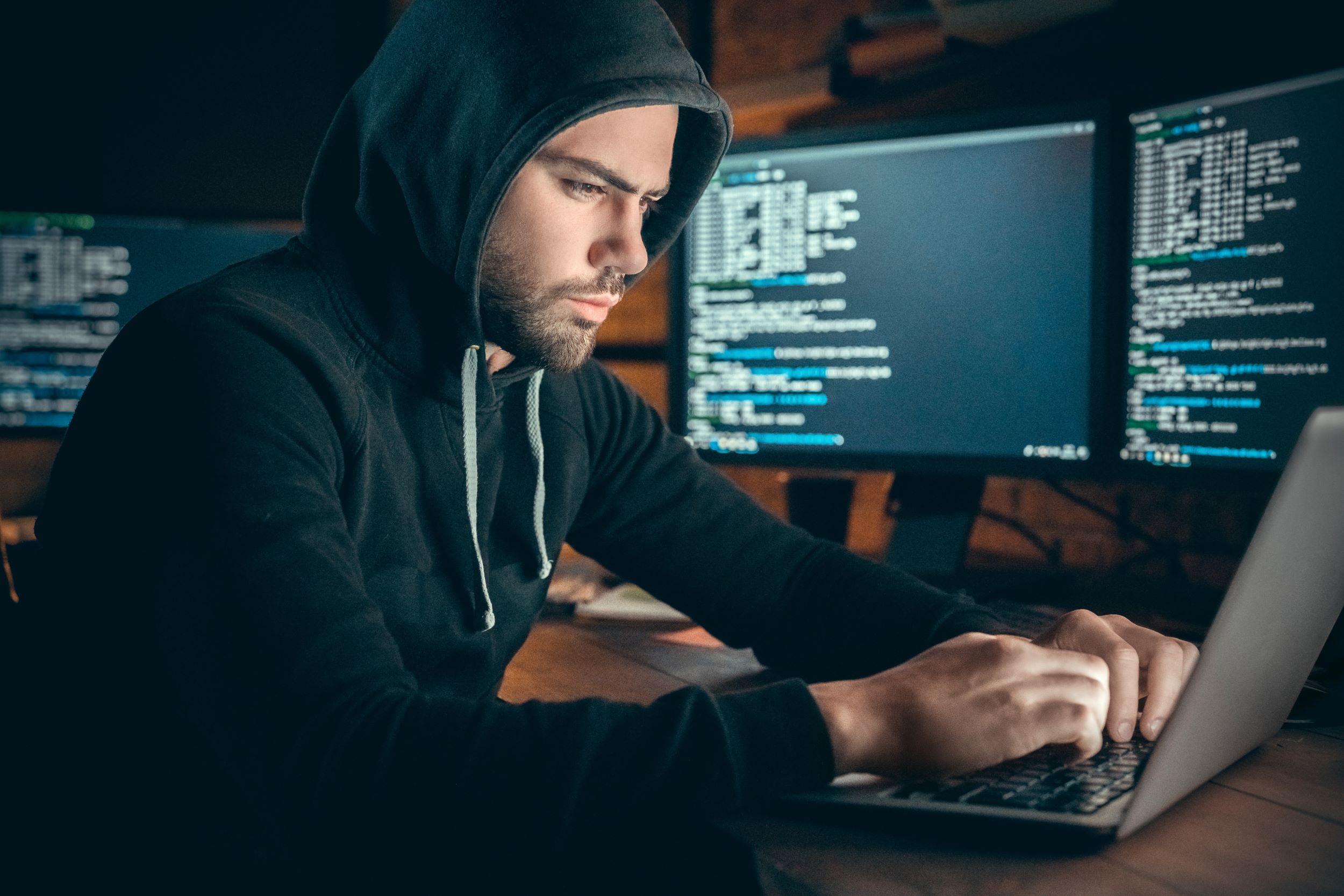 Man sitting with computer and screens with codings on.