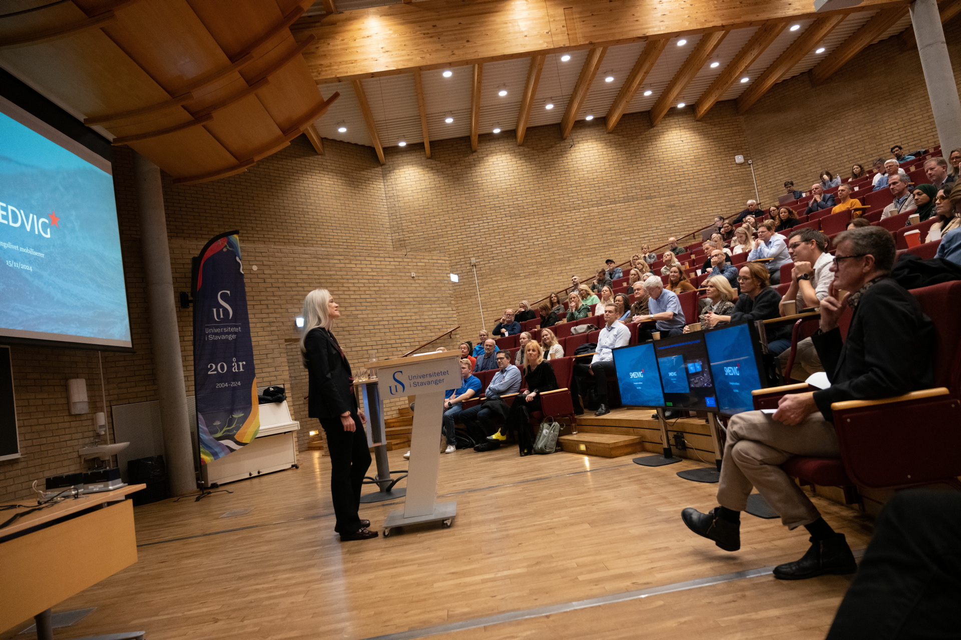 Mennesker i et auditorium som hører på en foredragsholder.