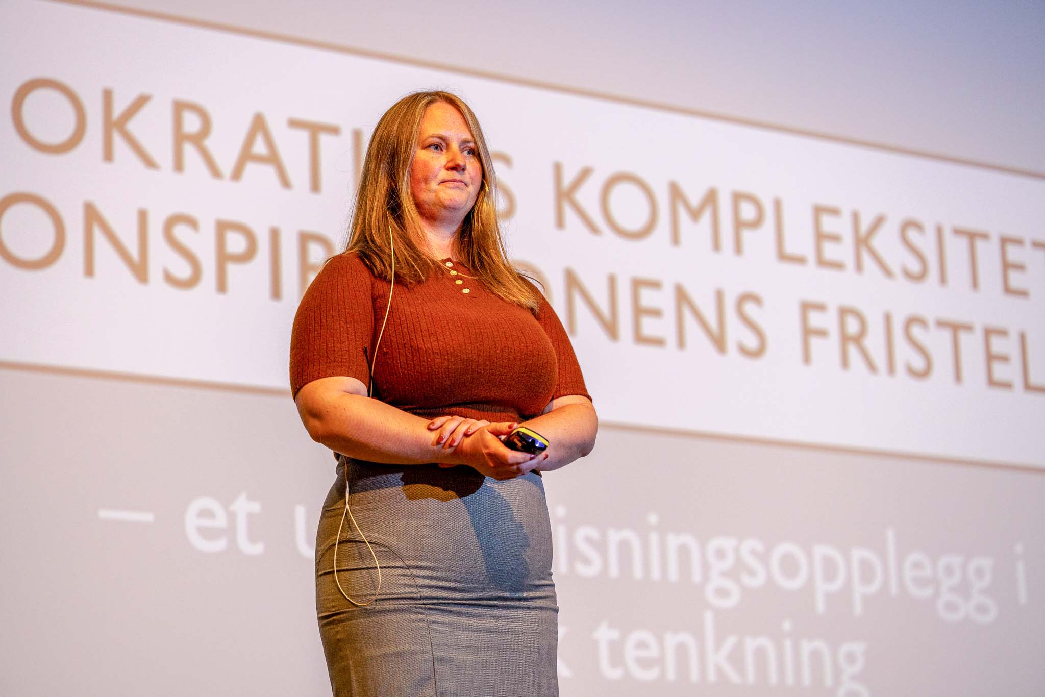 kvinne står foran en stor skjerm hvor vi ser teksten "Demokratiets kompleksitet".