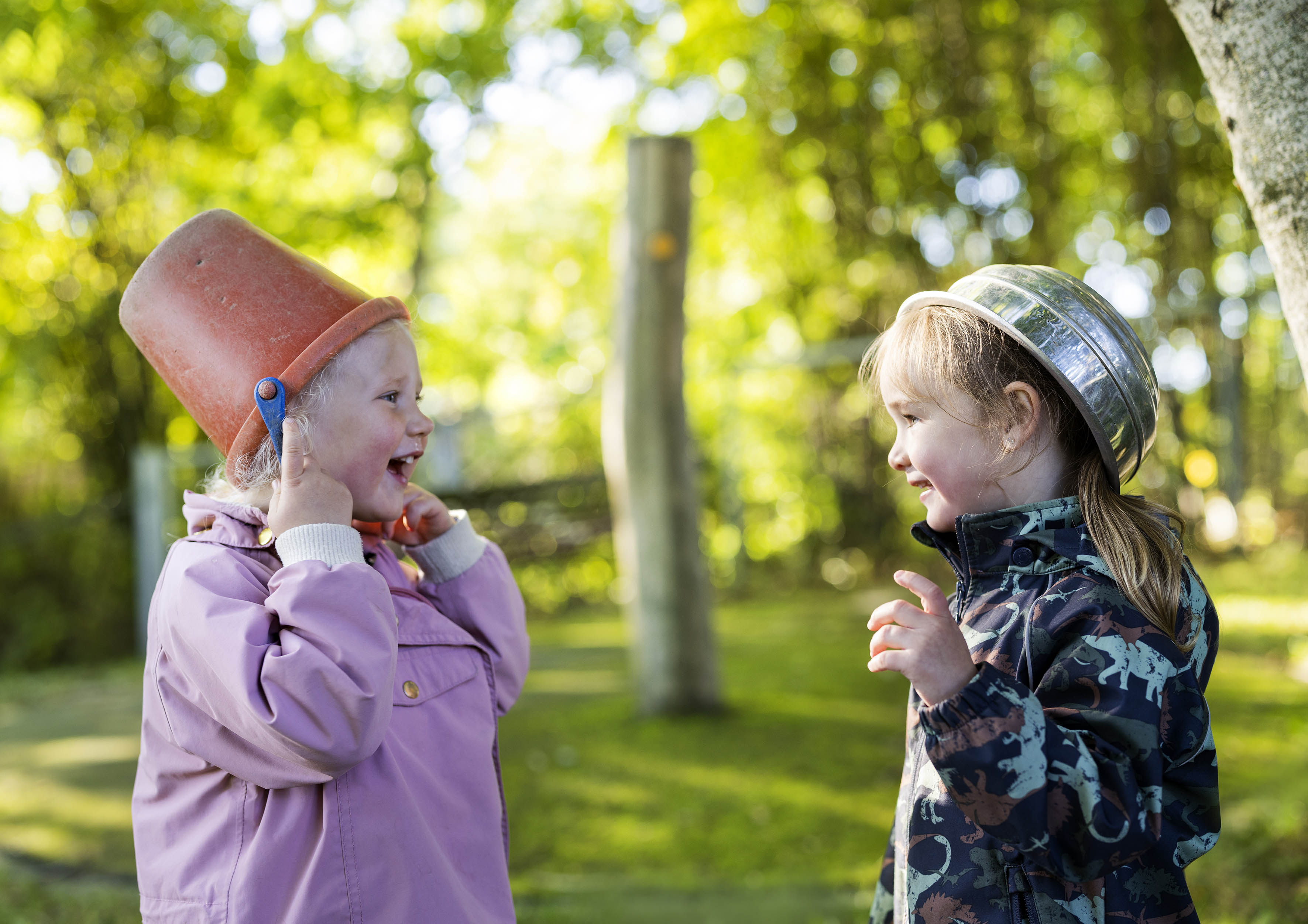 To jenter i barnehagealder ser på hverandre og smiler i skogen.