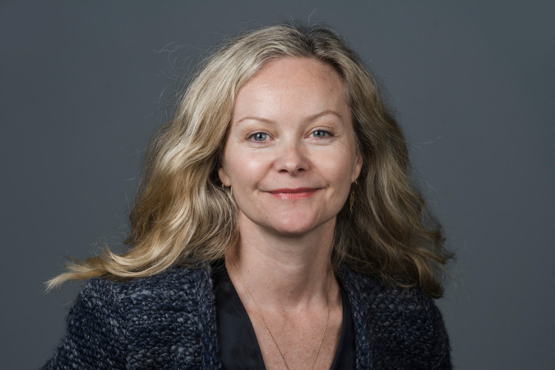 Kvinne med lyst hår foran en mørk vegg