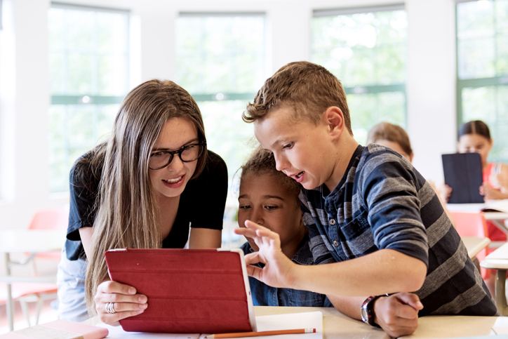 kvinne og to gutter ser på en ipad i et klasserom