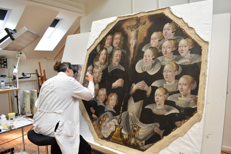 Malerikonservator i hvit frakk og med lupe arbeider med detalj på portrett