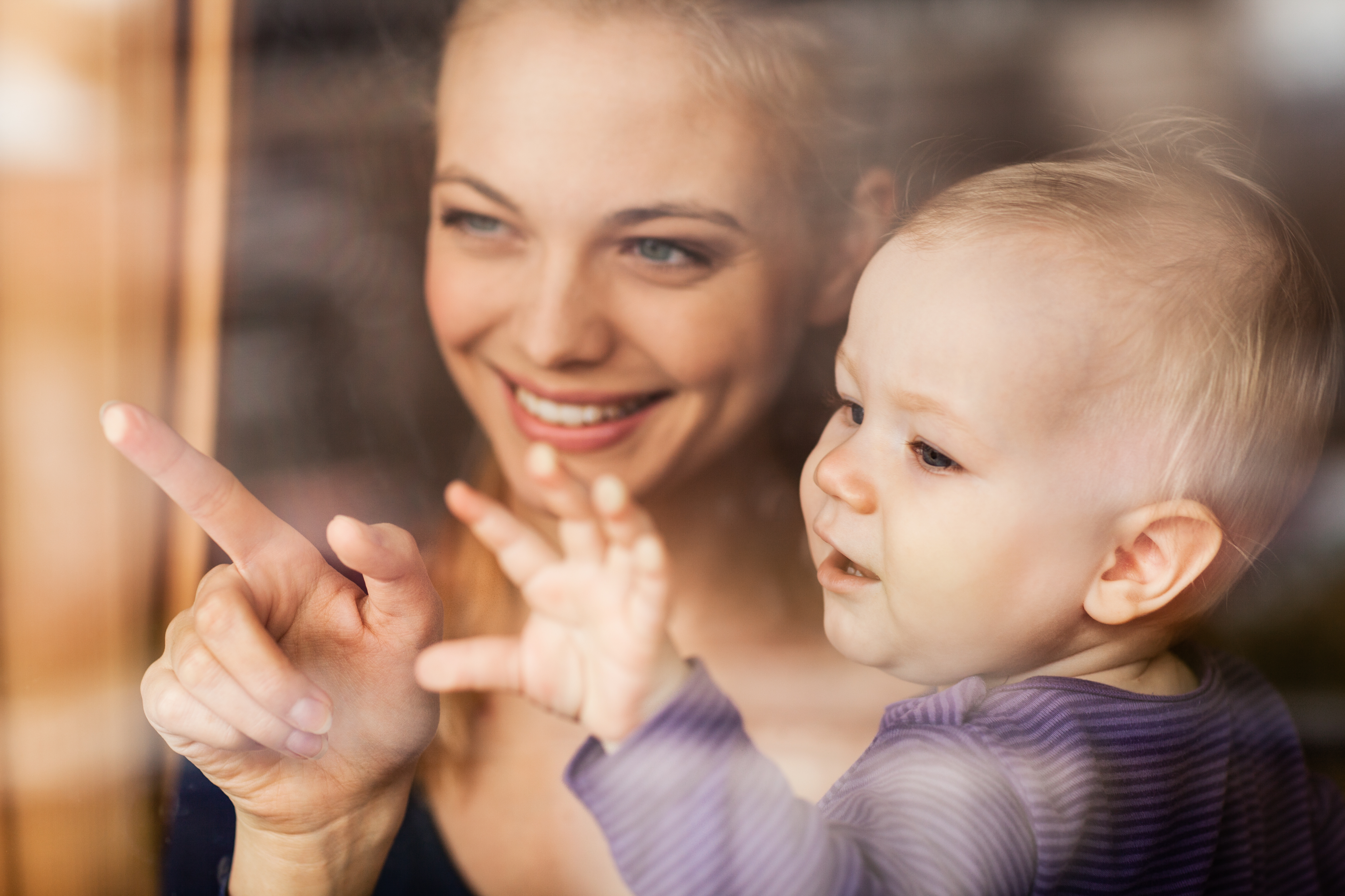 En kvinne holder et lite barn og peker ut gjennom et vindu