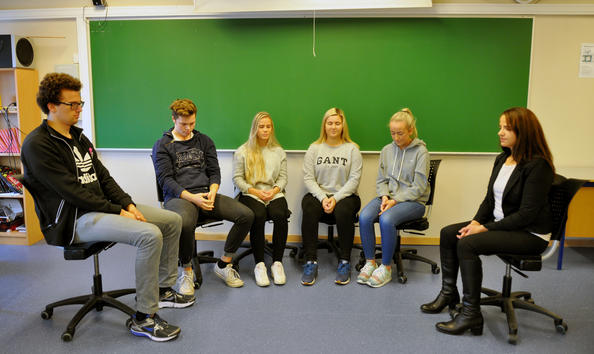 Fem elever sitter sammen med Kjersti Tharaldsen i et klasserom. De har samlet stolene foran tavla, og sitter med lukkede øyne mens de øver på oppmerksomt nærvær.