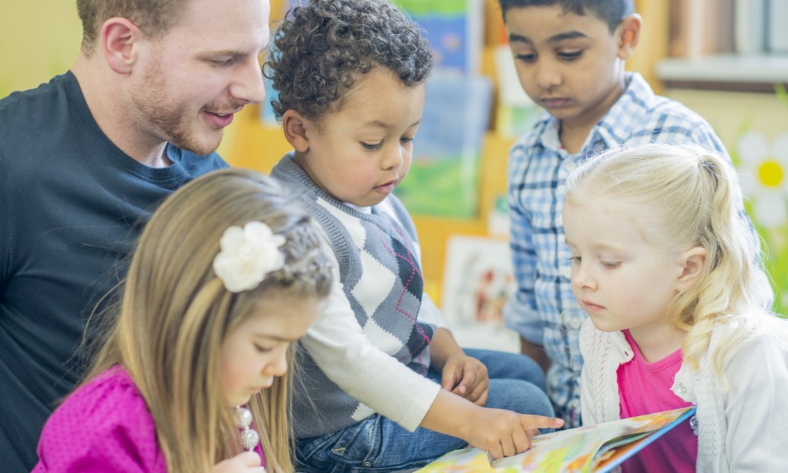 Mannlig barnehagelærer leser sammen med fire barn