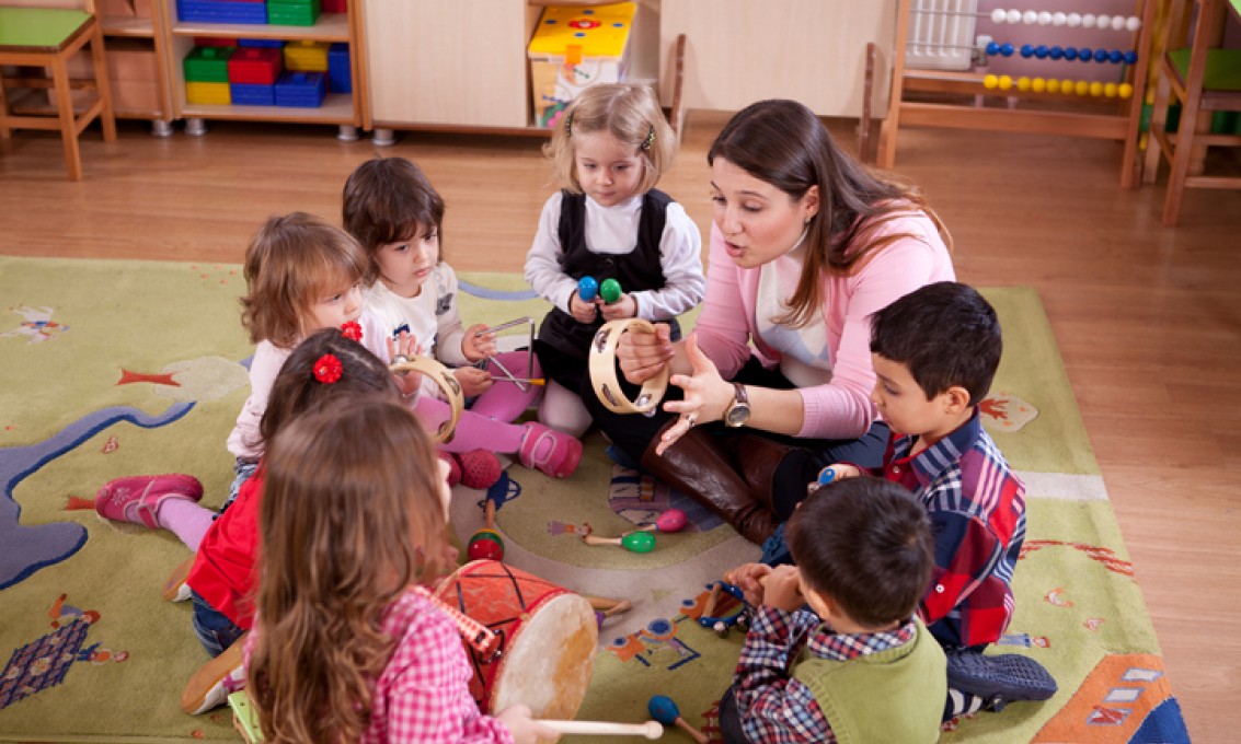 Gruppe med barnehagebarn sitter på golvet sammen med barnehagelærer