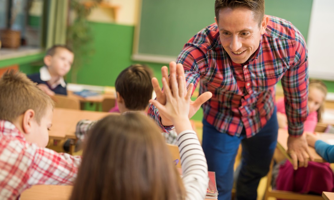 Mannlig lærer gir "high five" til en ung barneskoleelev i et klasserom