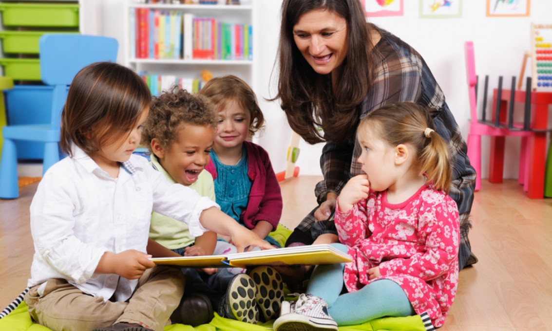 Barnehagelærer og fire barn leser bok sammen