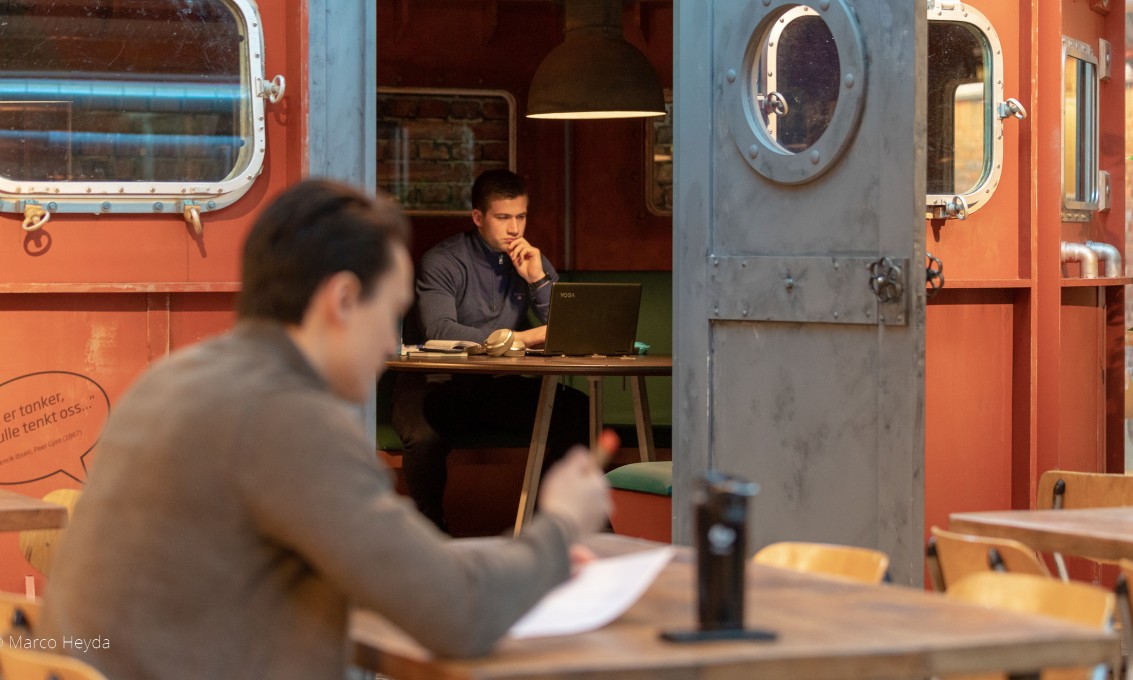 En student studerer ved et bord, mens en annen student studerer i en av tankene i Dataverkstedet