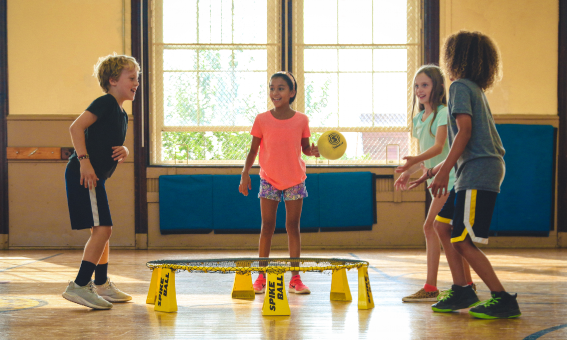 Fire barn leker med en gul ball inne i en gymsal