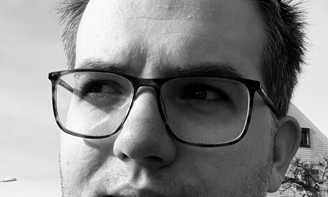 Portrett i svart-hvitt av ing herre med briller som ser skrått vekk fra fotograf