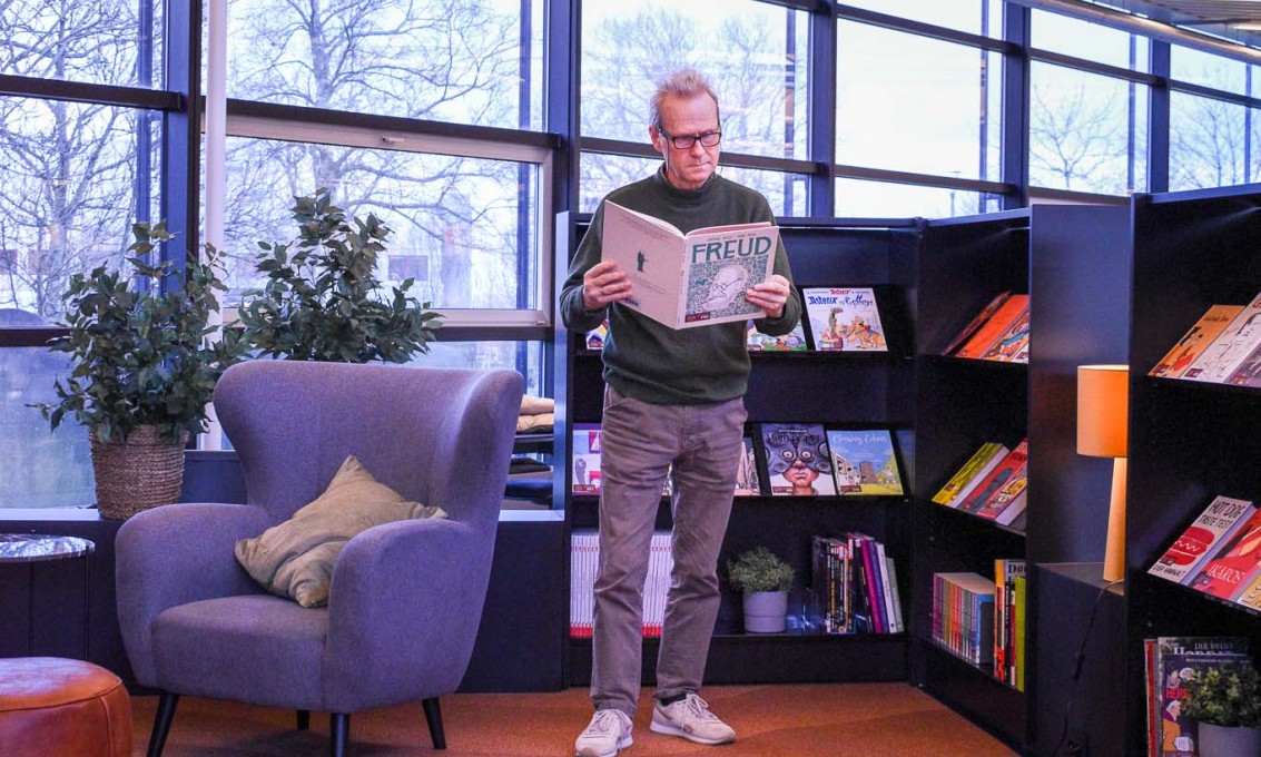 Mann står å leser tegneserie om Freud ved siden av en bokhylle og en lenestol