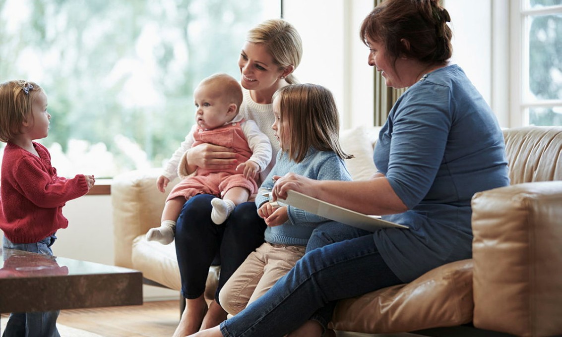 Illustrasjonsbilde av arbeidet til en helsesykepleier. På bildet ser du en mor, en helsesykepleier og tre barn.