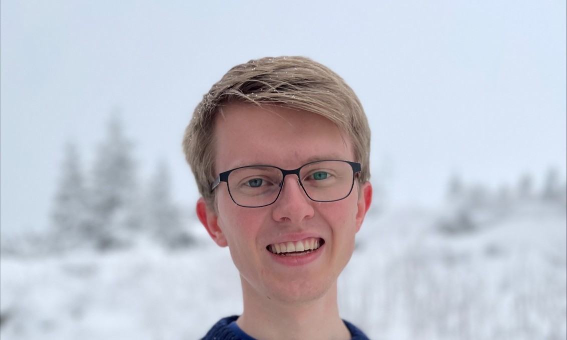 Ung mann med briller og ullgenser står utendørs med snø i håret