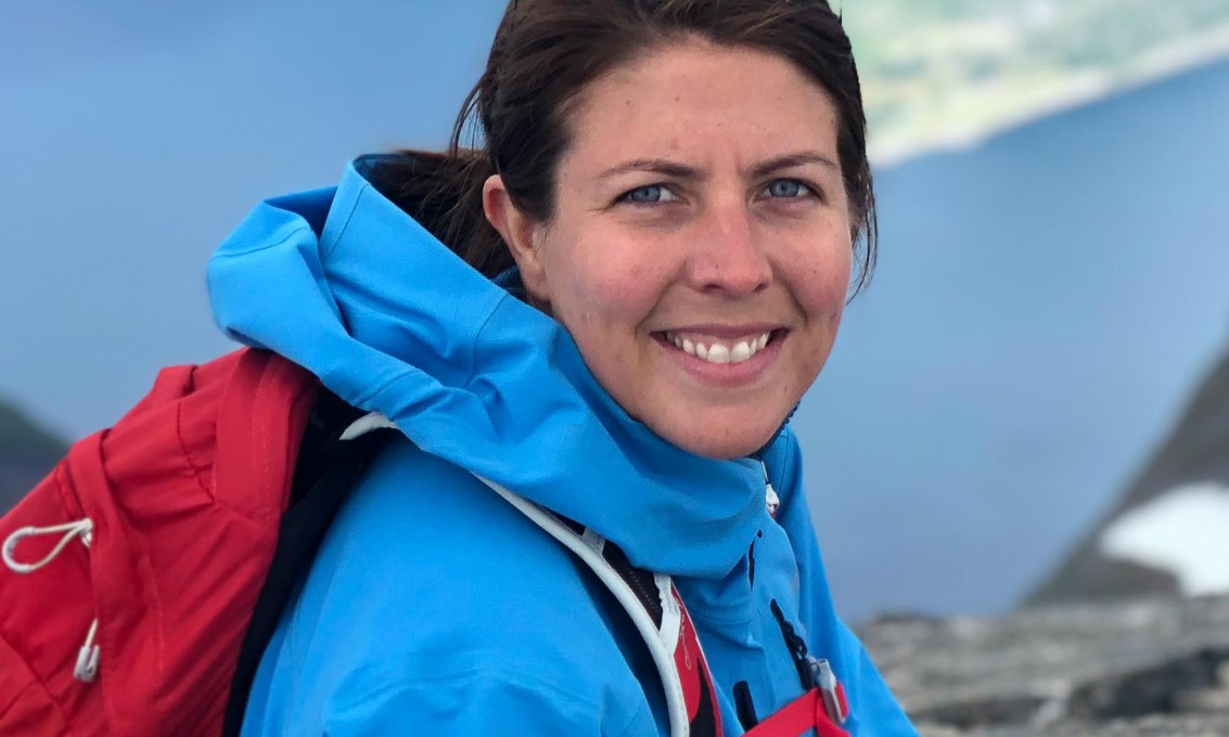 Kvinne med blå jakke og rød ryggsekk tar pause på fjelltur