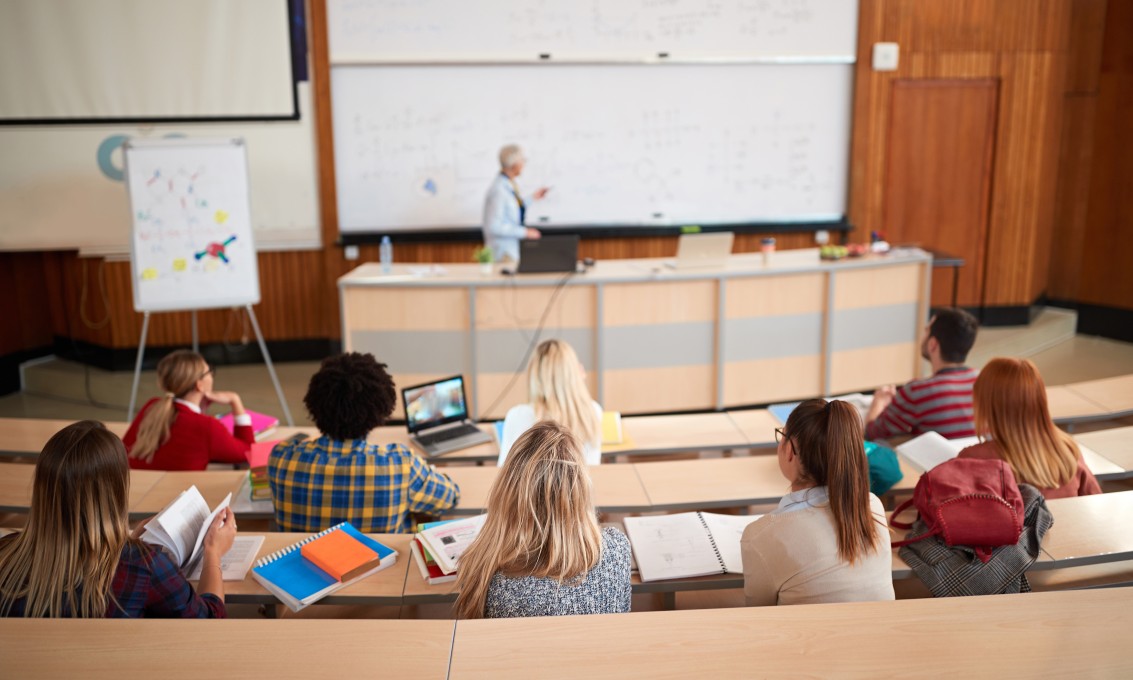 Studenter i auditorium sett bakfra med foreleser i bakgrunnen